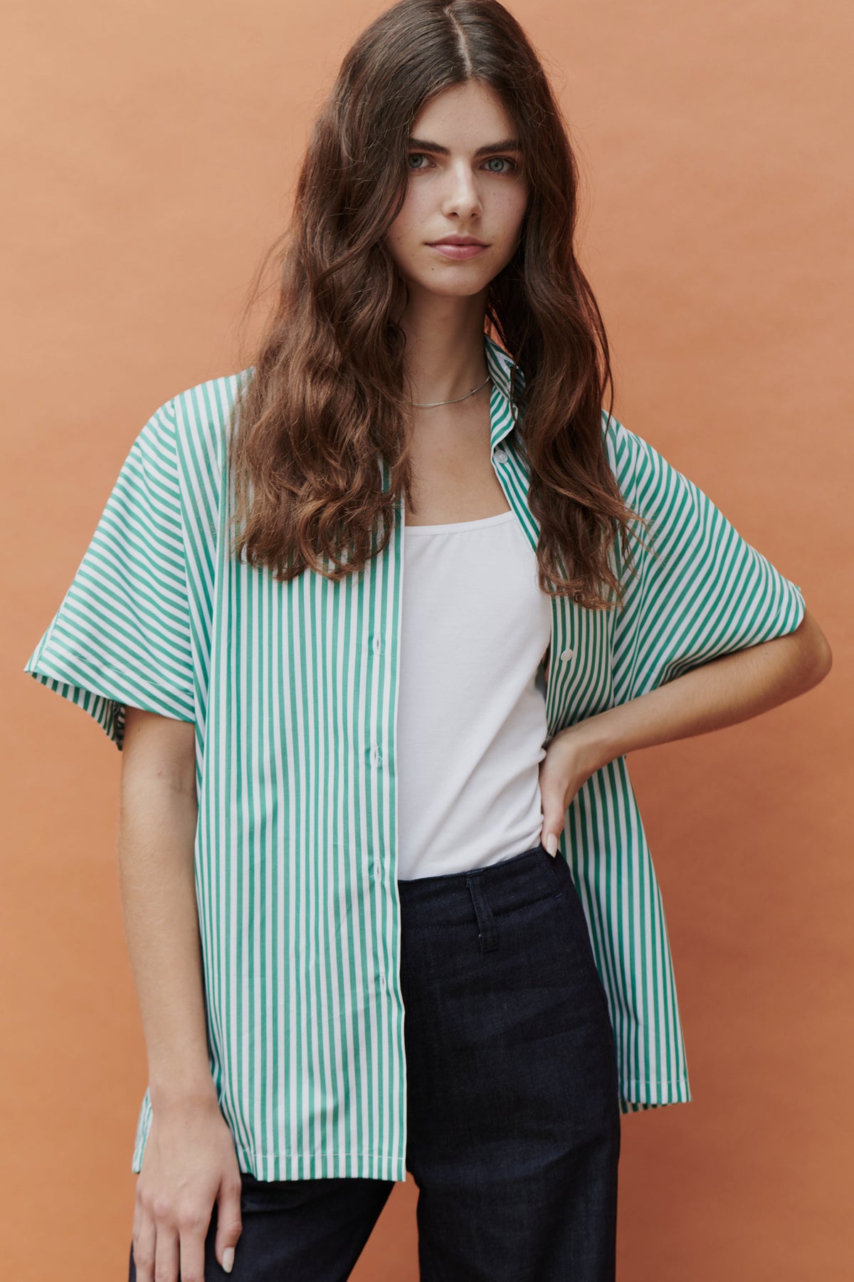 woman with hand on her hip wearing green and white short sleeve shirt over a white camisole