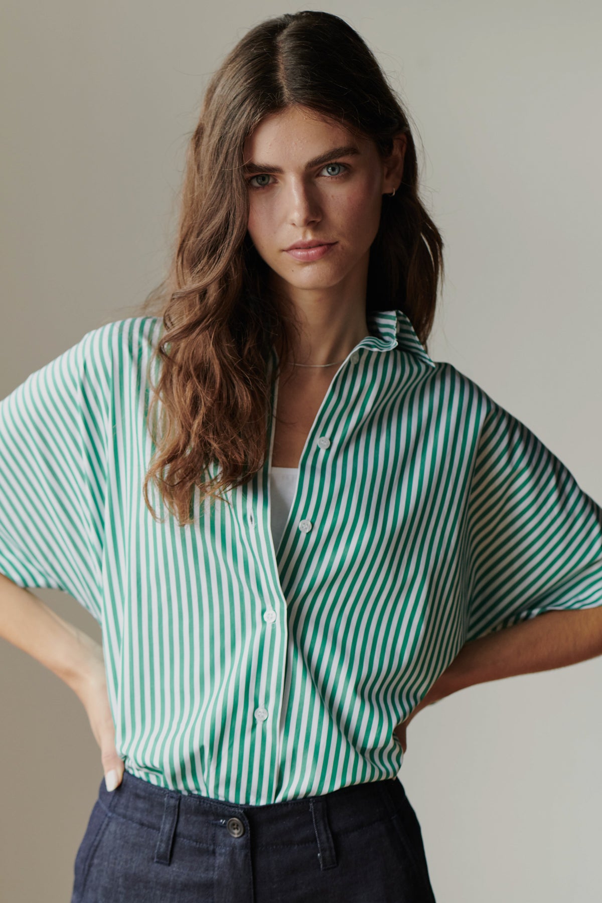 woman with blank expression wearing a green and white short sleeved shirt with hands on her hips