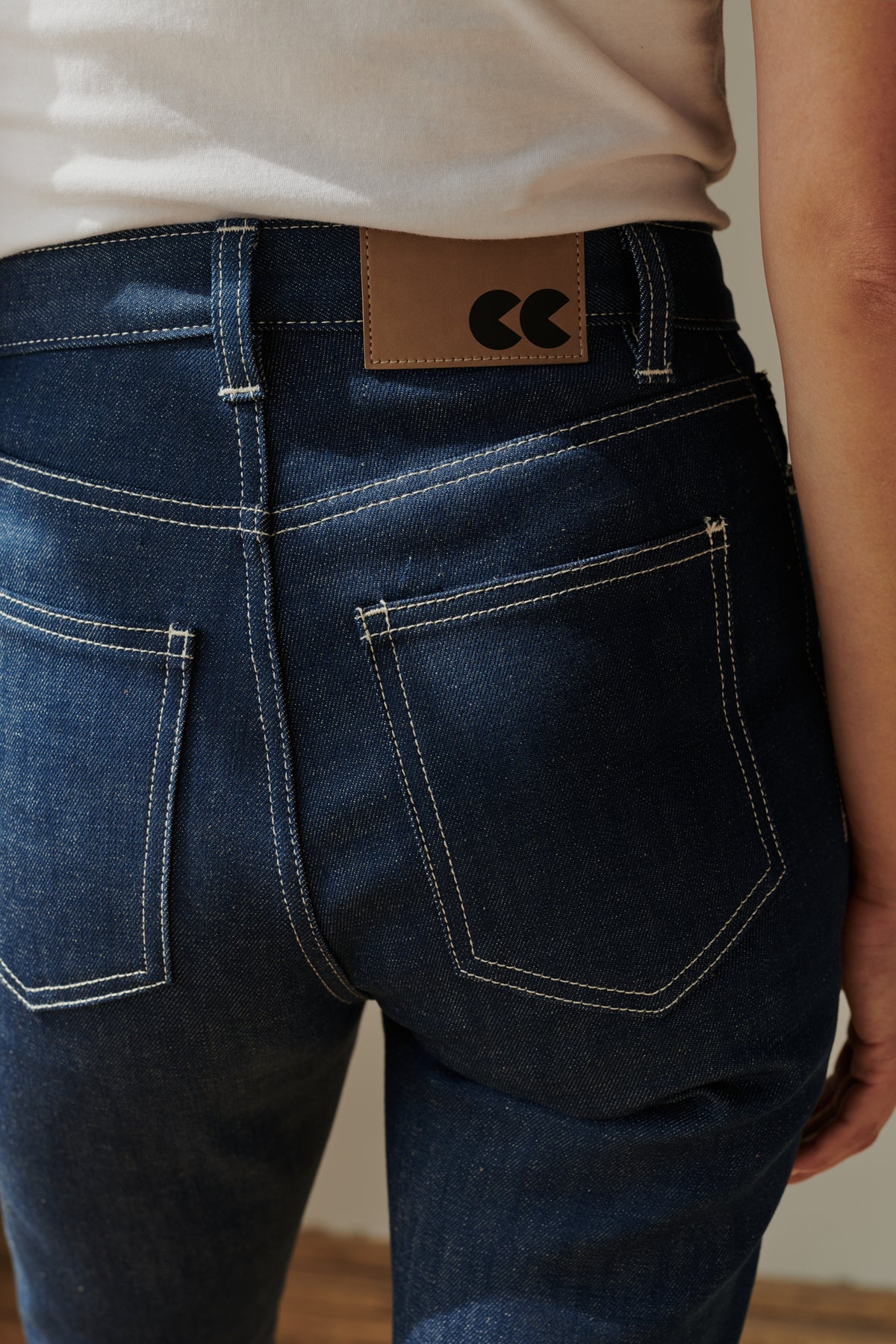 Back pocket and belt loop detail of female wearing straight leg high rise jean in blue.