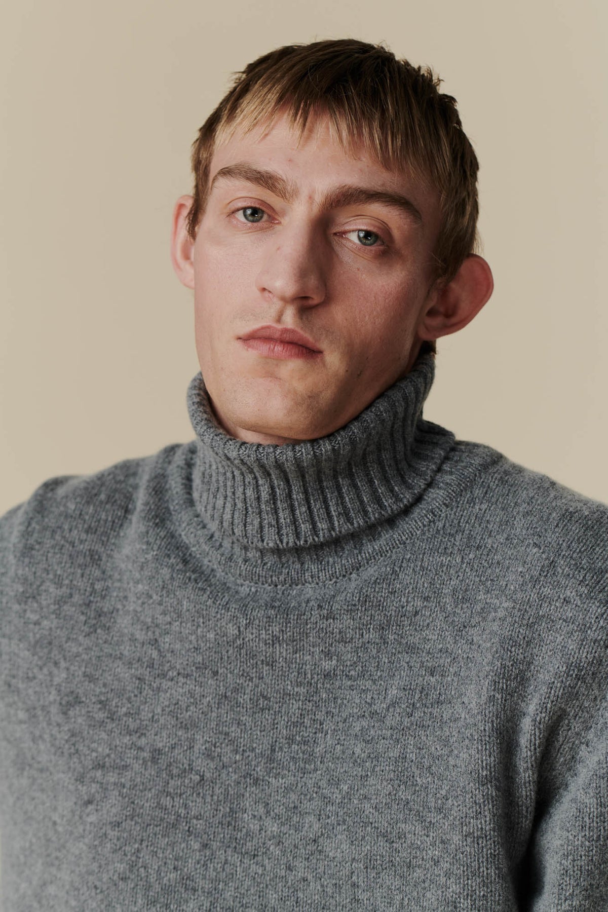 Portrait shot of dirty blonde, white male wearing grey roll neck jumper