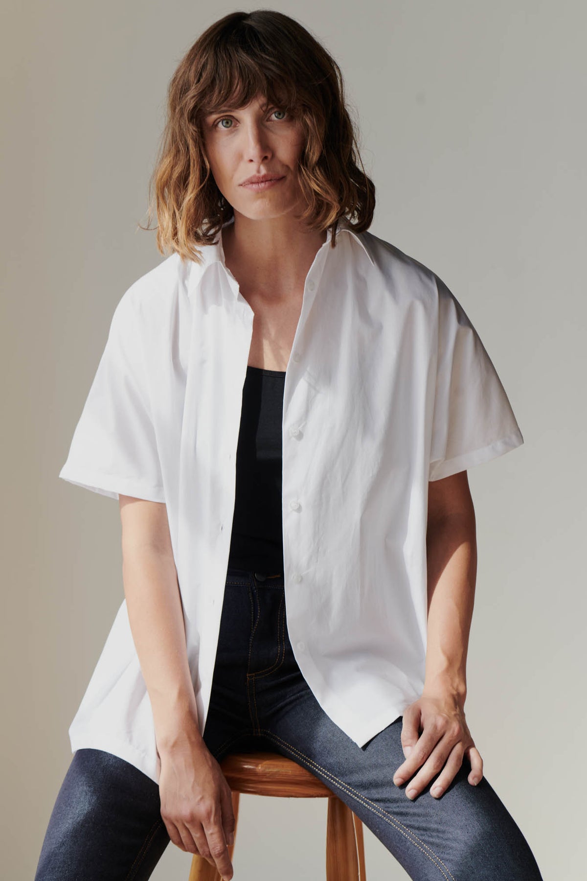 Female wearing Ava short sleeve shirt in white unbuttoned over black camisole 