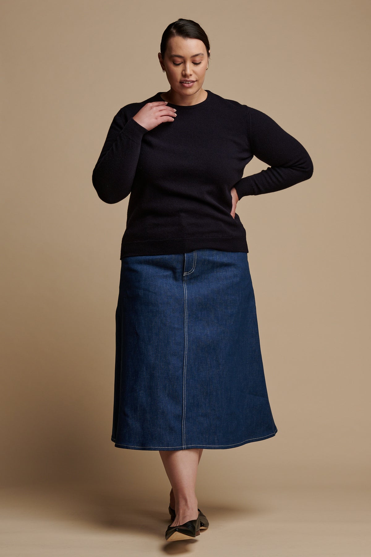 Female with brown hair tied back looking to the ground wearing Bobbie A line denim midi skirt in blue paired with lambswool crew neck in navy.