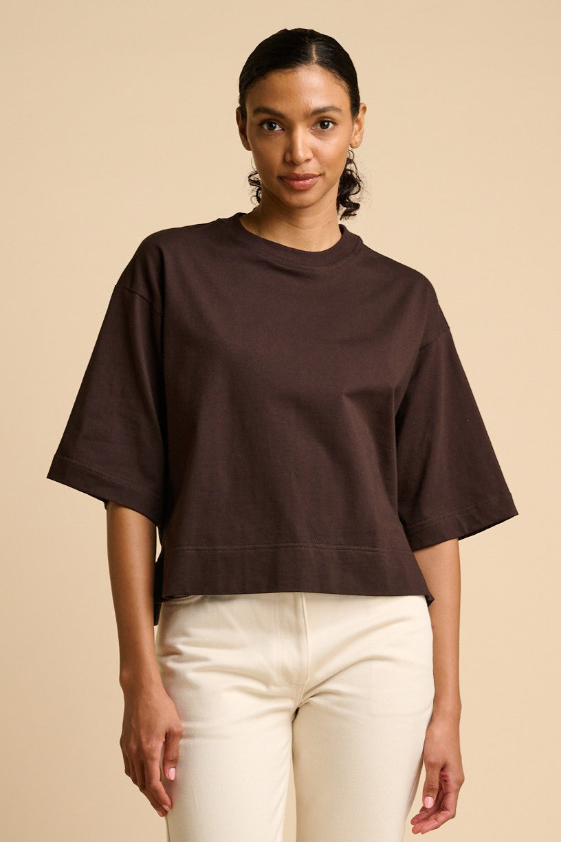 Woman wearing a brown t-shirt and white pants on a beige background