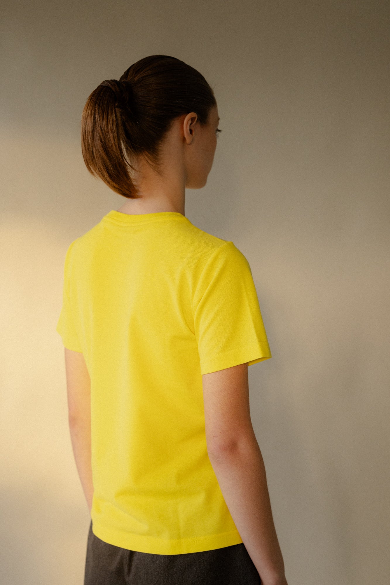 Thigh up image of smiley female wearing women's breathable short sleeve t shirt plastic free in canary yellow with white CCOA logo