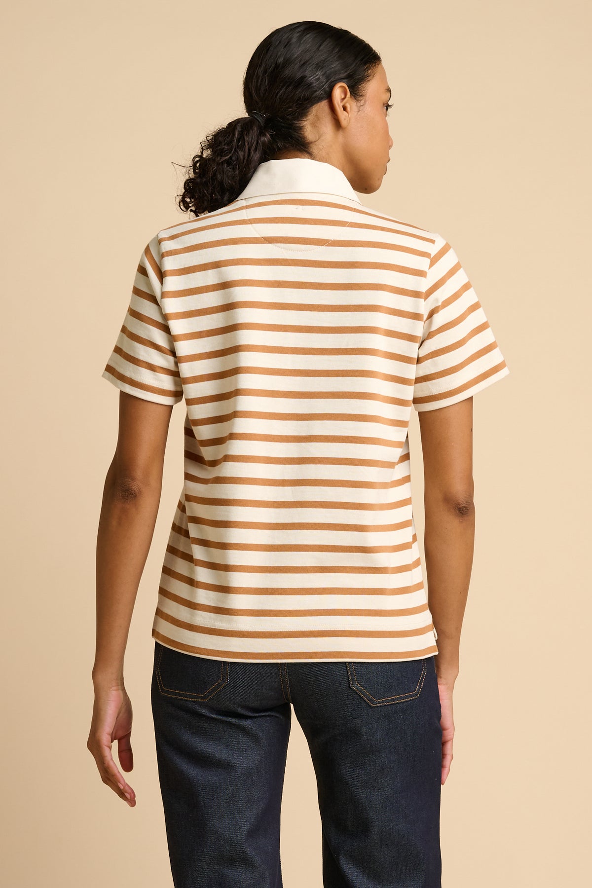Woman wearing a striped polo shirt and jeans on a beige background.