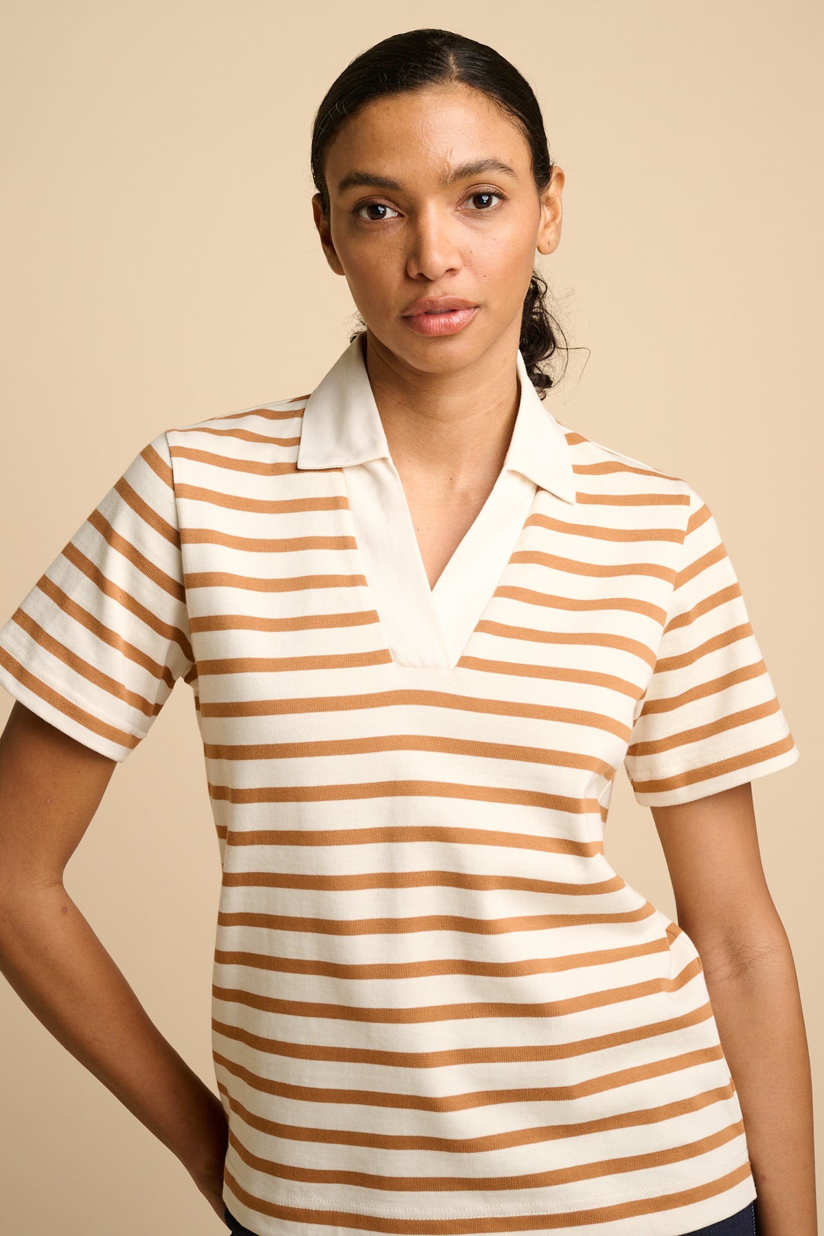 Woman wearing a striped polo shirt against a beige background