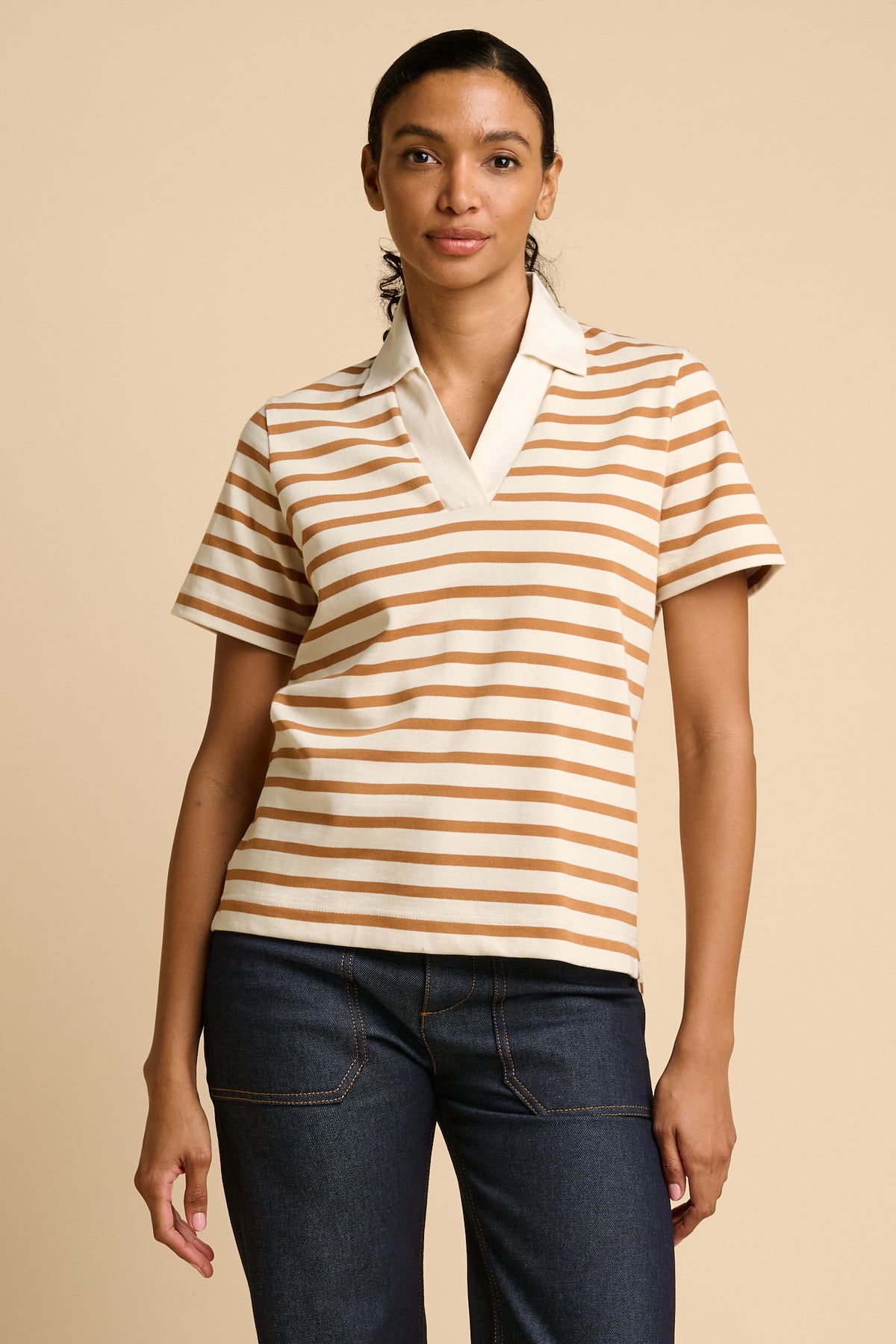 Woman wearing a striped polo shirt and jeans on a beige background.