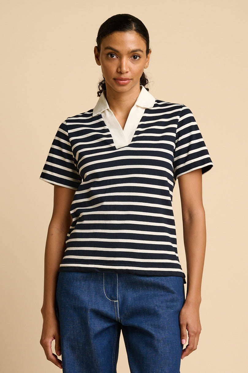 Woman wearing a navy and ecru striped polo shirt with a beige background.