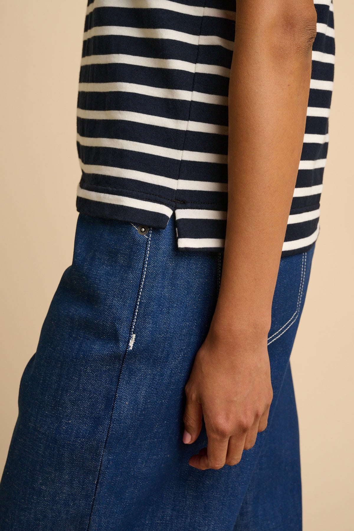 Person wearing a navy and ecru striped shirt with blue jeans on a beige background.