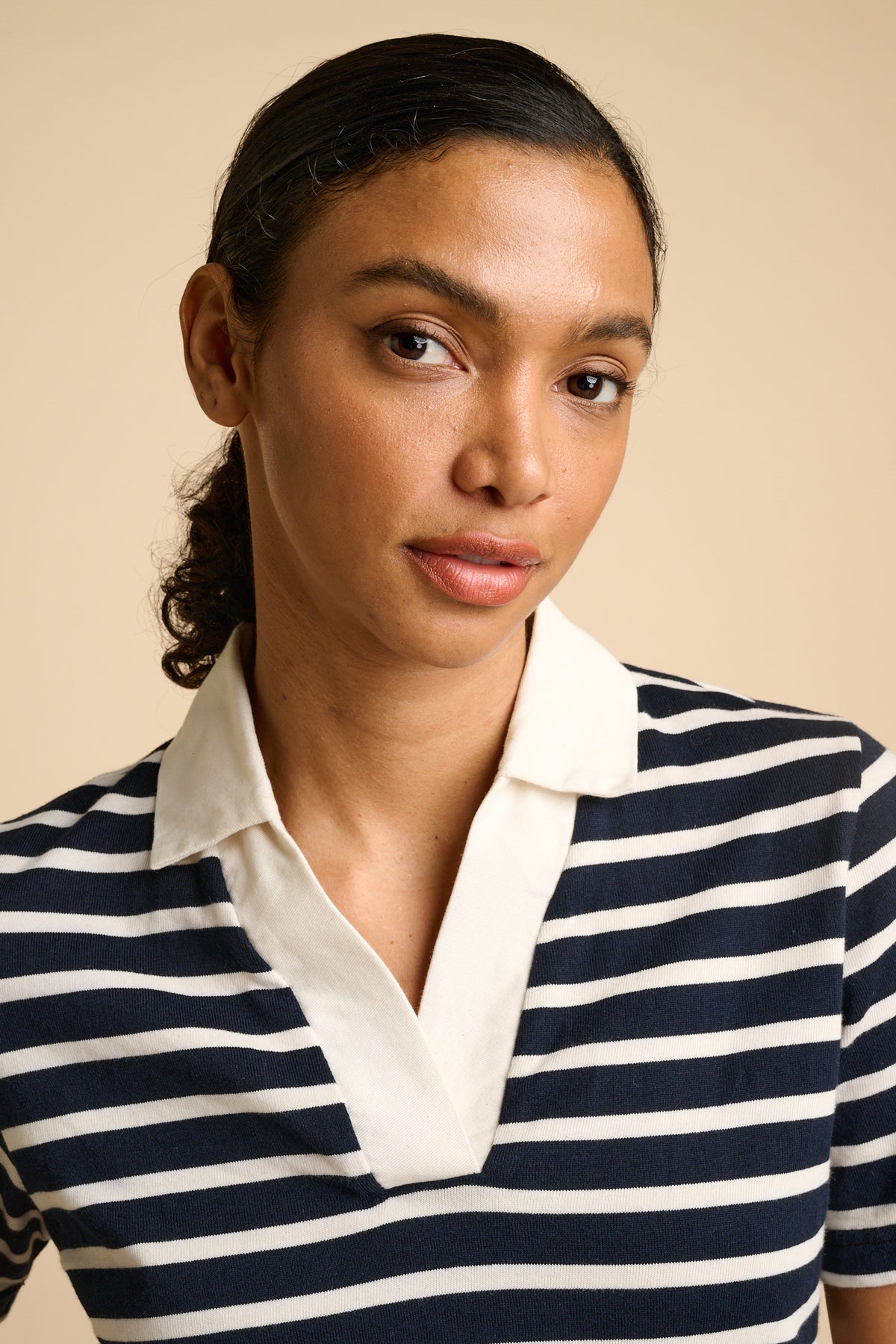 Woman wearing a navy and ecru striped  top with collar against a beige background.