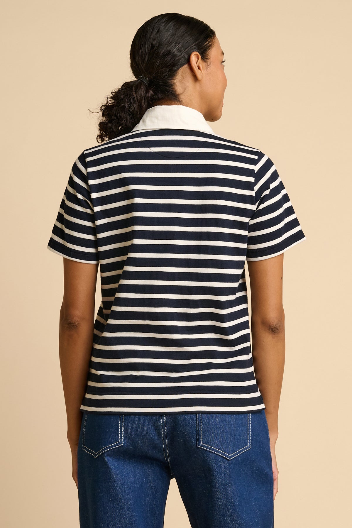 Woman wearing a navy and ecru striped polo shirt with a beige background.