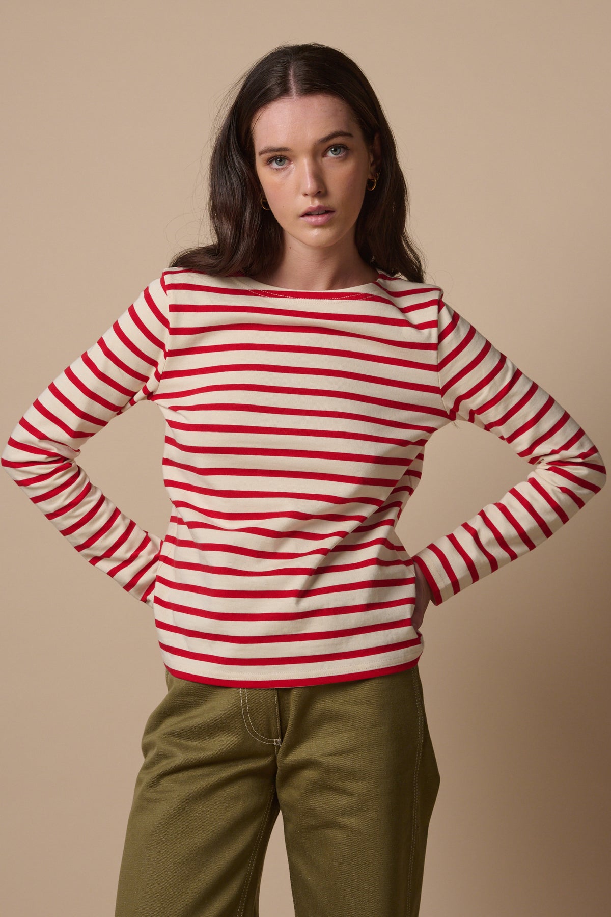 Thigh up image of white female with long brunette hair wearing Breton in ecru and red with hands on hips