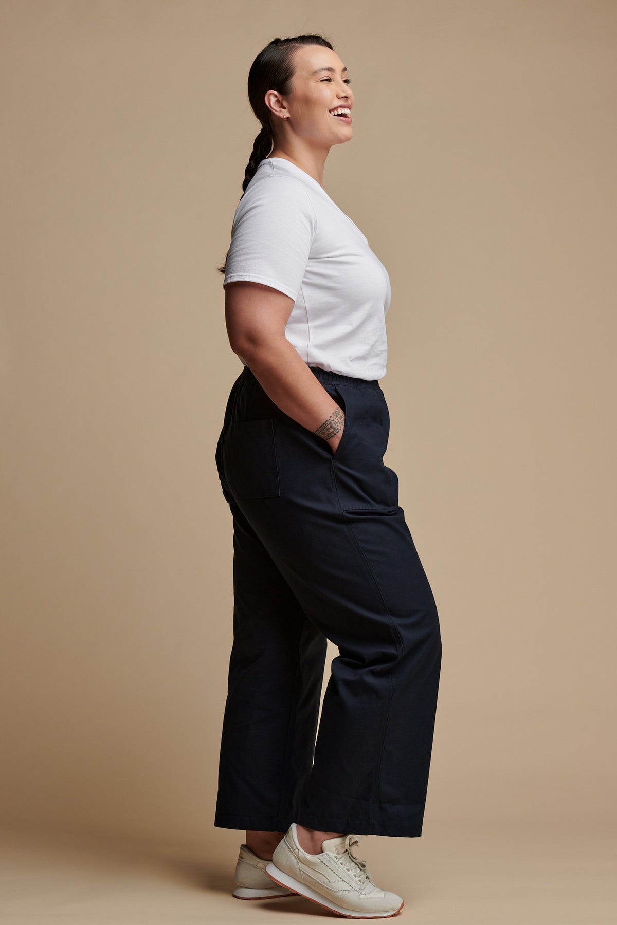 The side of female wearing drawstring tapered cotton canvas trousers in navy with her hand in the front pocket, paired with v neck t shirt in white.