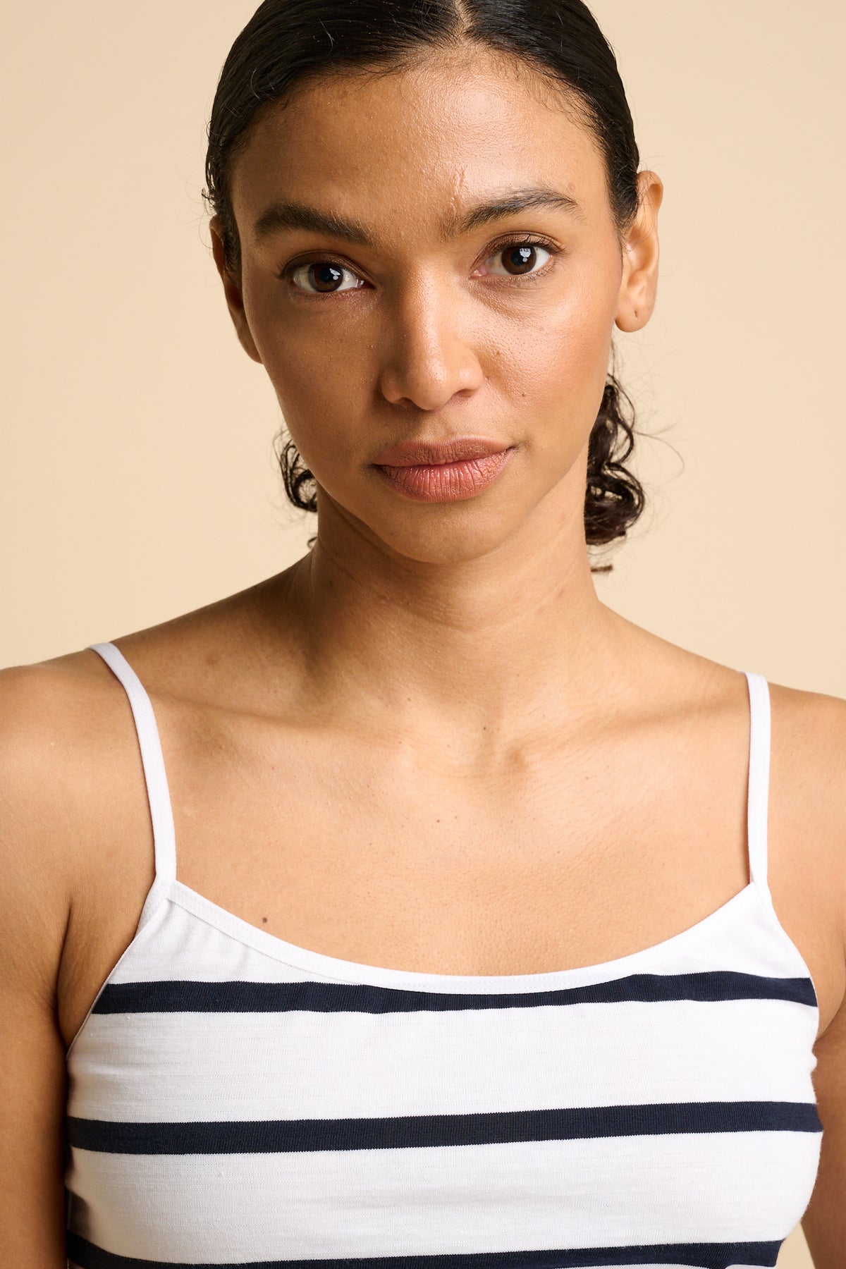 Woman wearing a striped camisole and denim shorts on a beige background