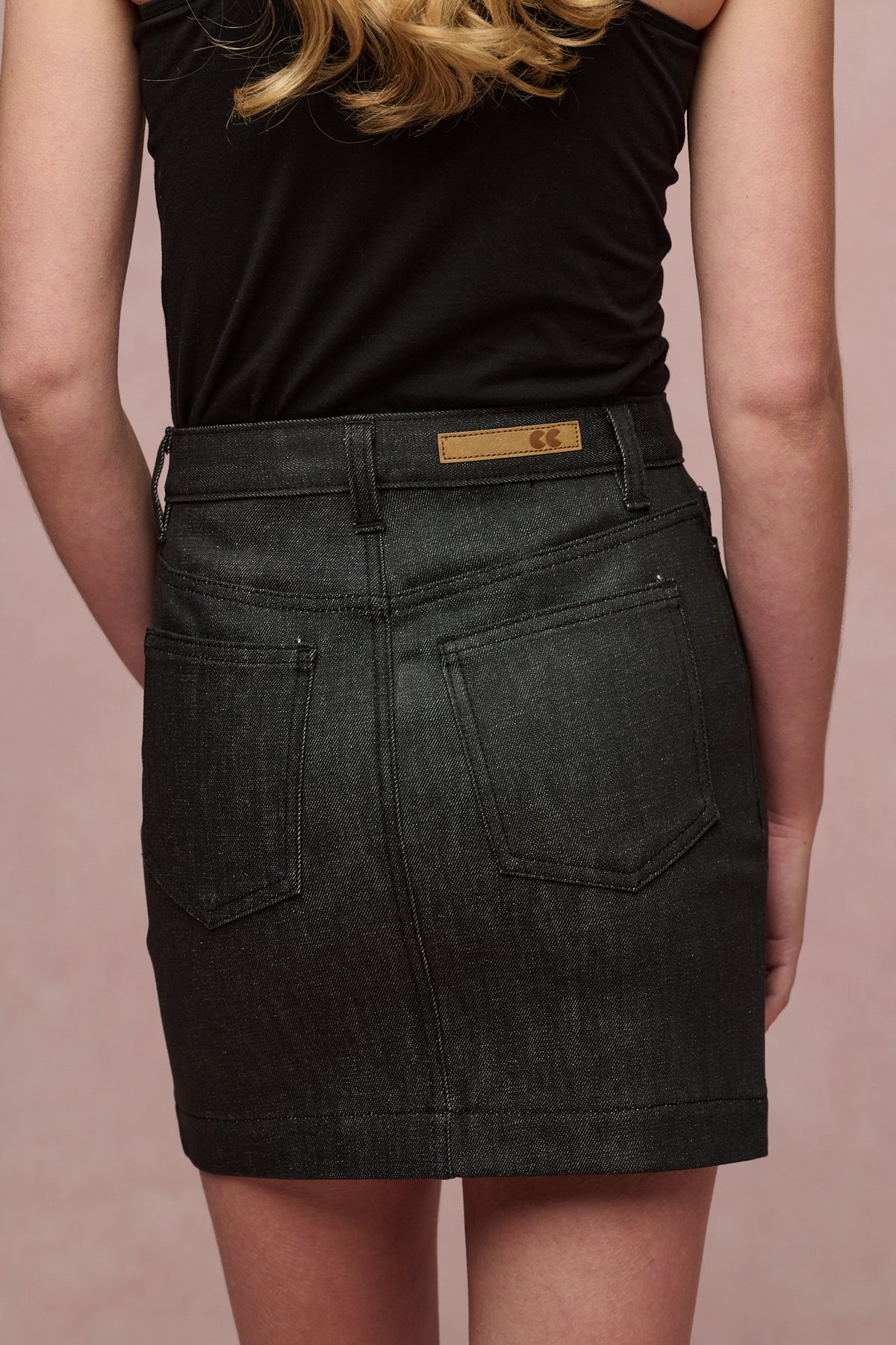 Image showing a close up of the back of Charlie denim mini skirt in black. Two back pockets, belt loops and CC logo jean patch on the waistband