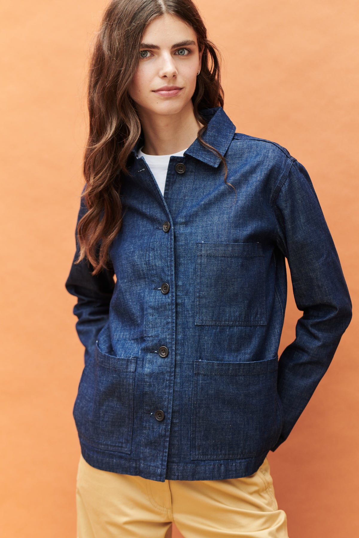Front, thigh up image of brunette female wearing buttonedchore jacket in denim
