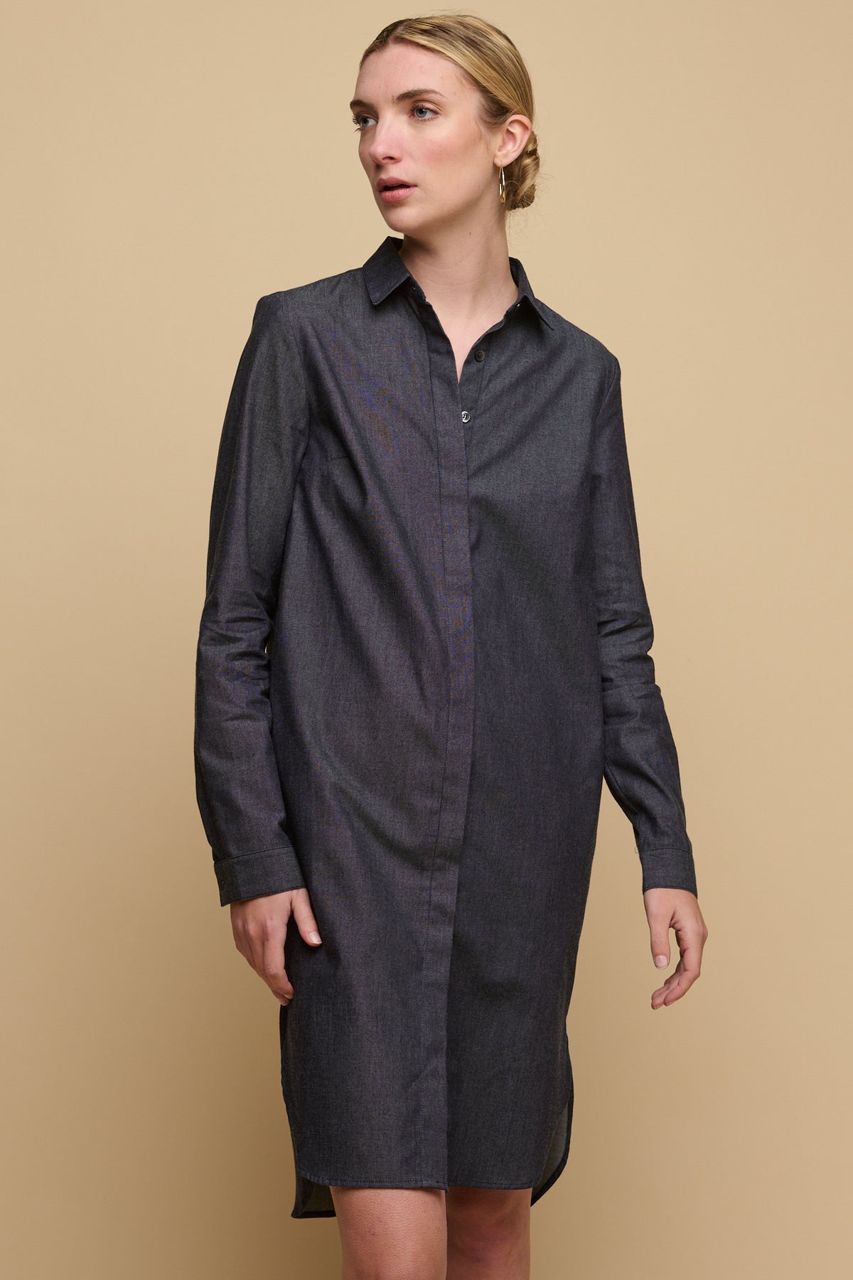 Knee up image of female wearing collared shirt dress in indigo with top three buttoned undone. 