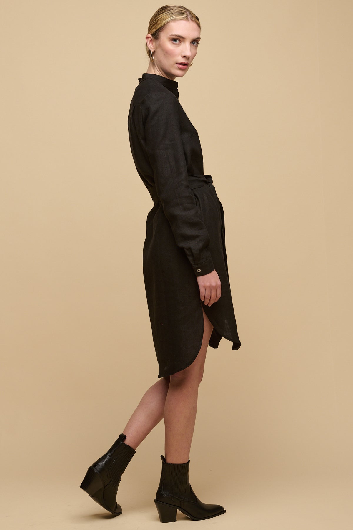 Full body side view of female wearing black linen collarless shirt dress