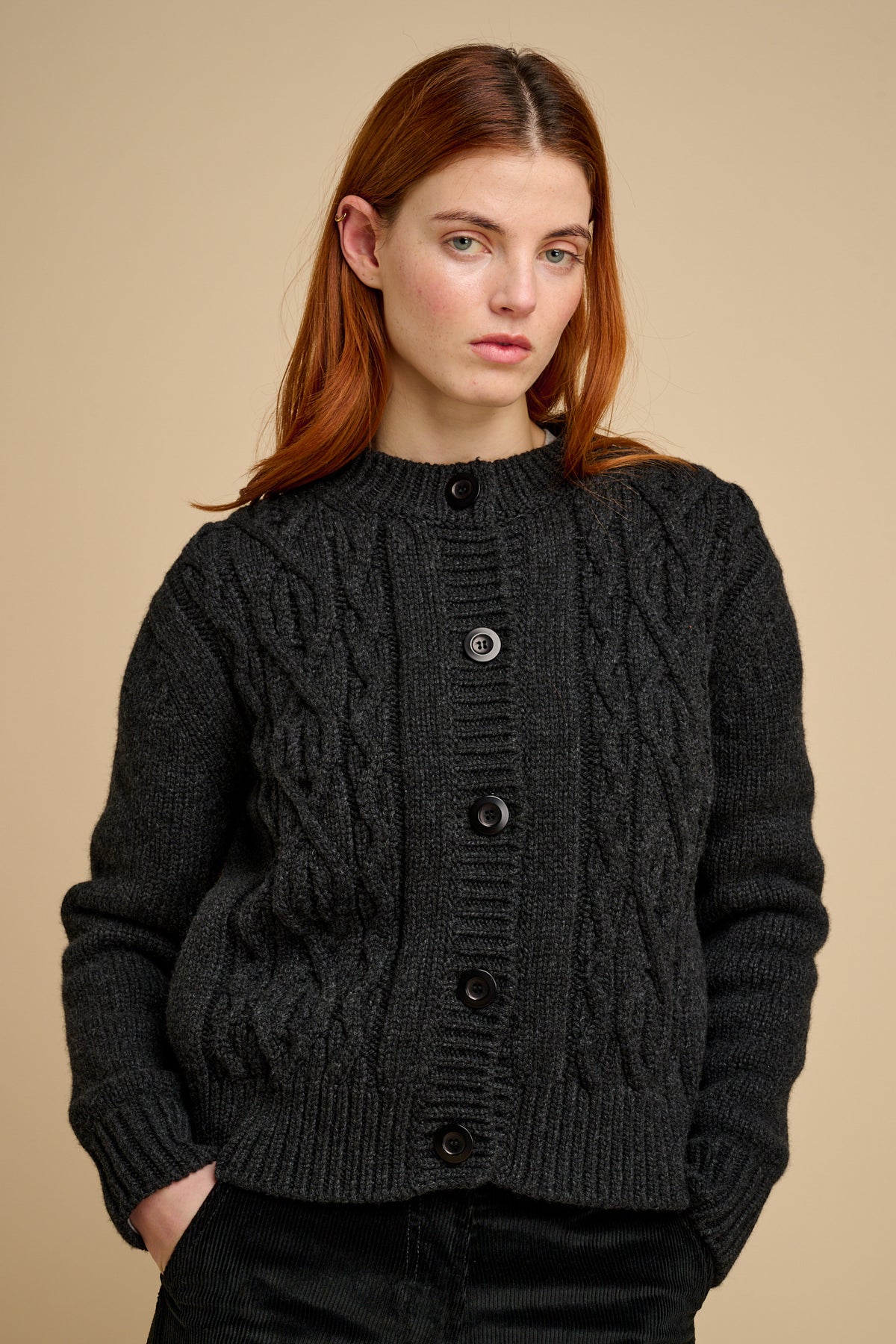 Woman wearing a dark grey knitted cardigan against a beige background