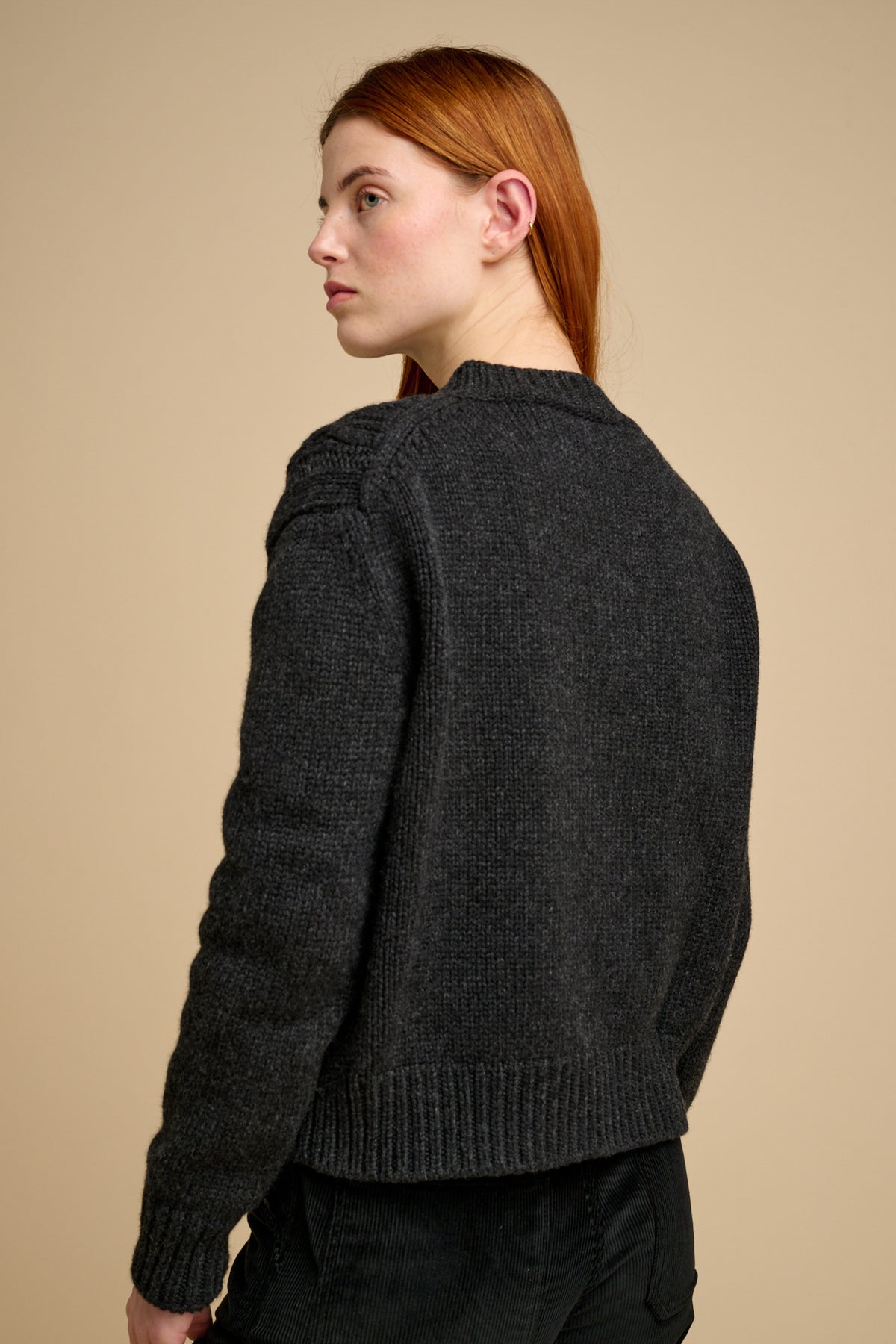 The back of woman wearing a dark grey knitted cardigan against a beige background