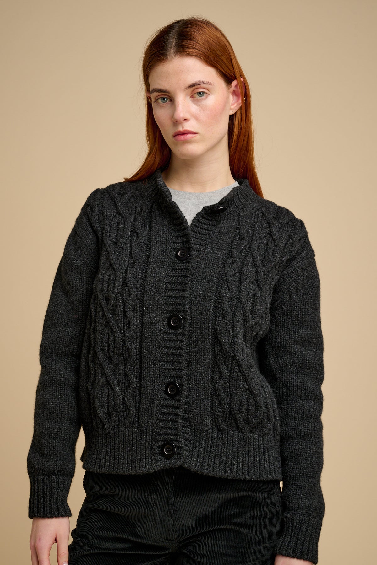 Woman wearing a dark grey cable knit cardigan on a beige background