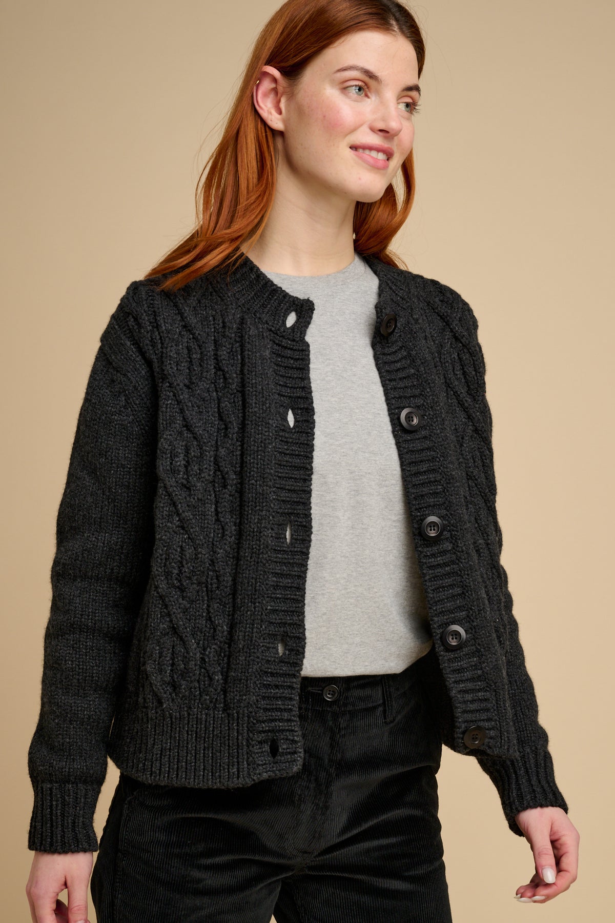 Woman wearing a dark grey cable knit cardigan over a grey t shirt on a beige background