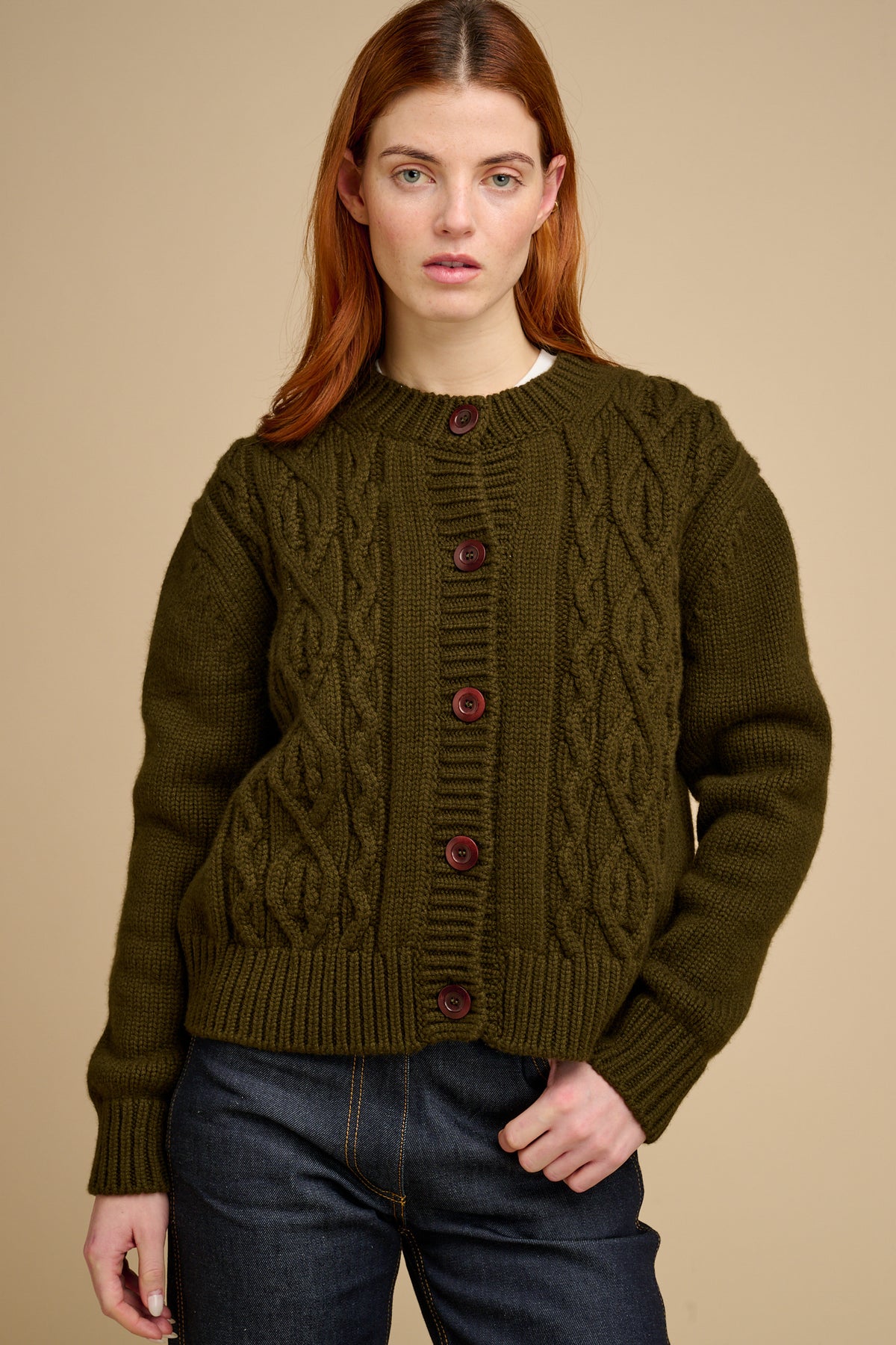 Woman wearing a green cable knit cardigan against a beige background