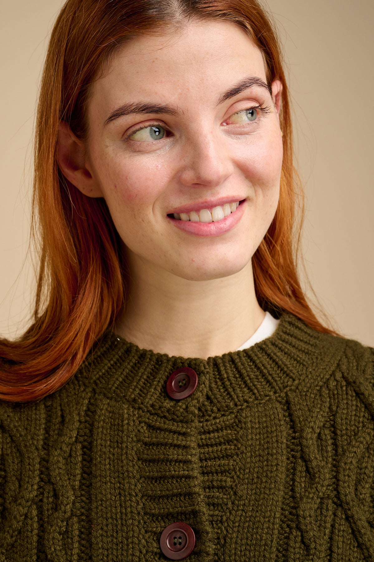 Woman wearing a green cable knit cardigan against a beige background