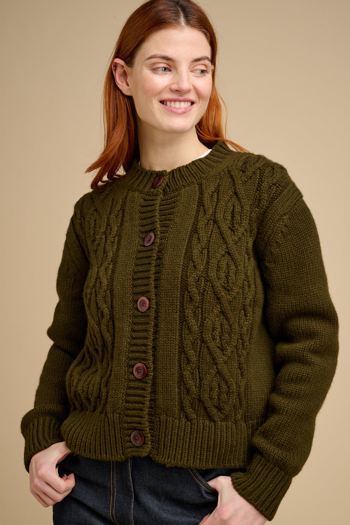 Woman wearing a green cable knit cardigan against a beige background