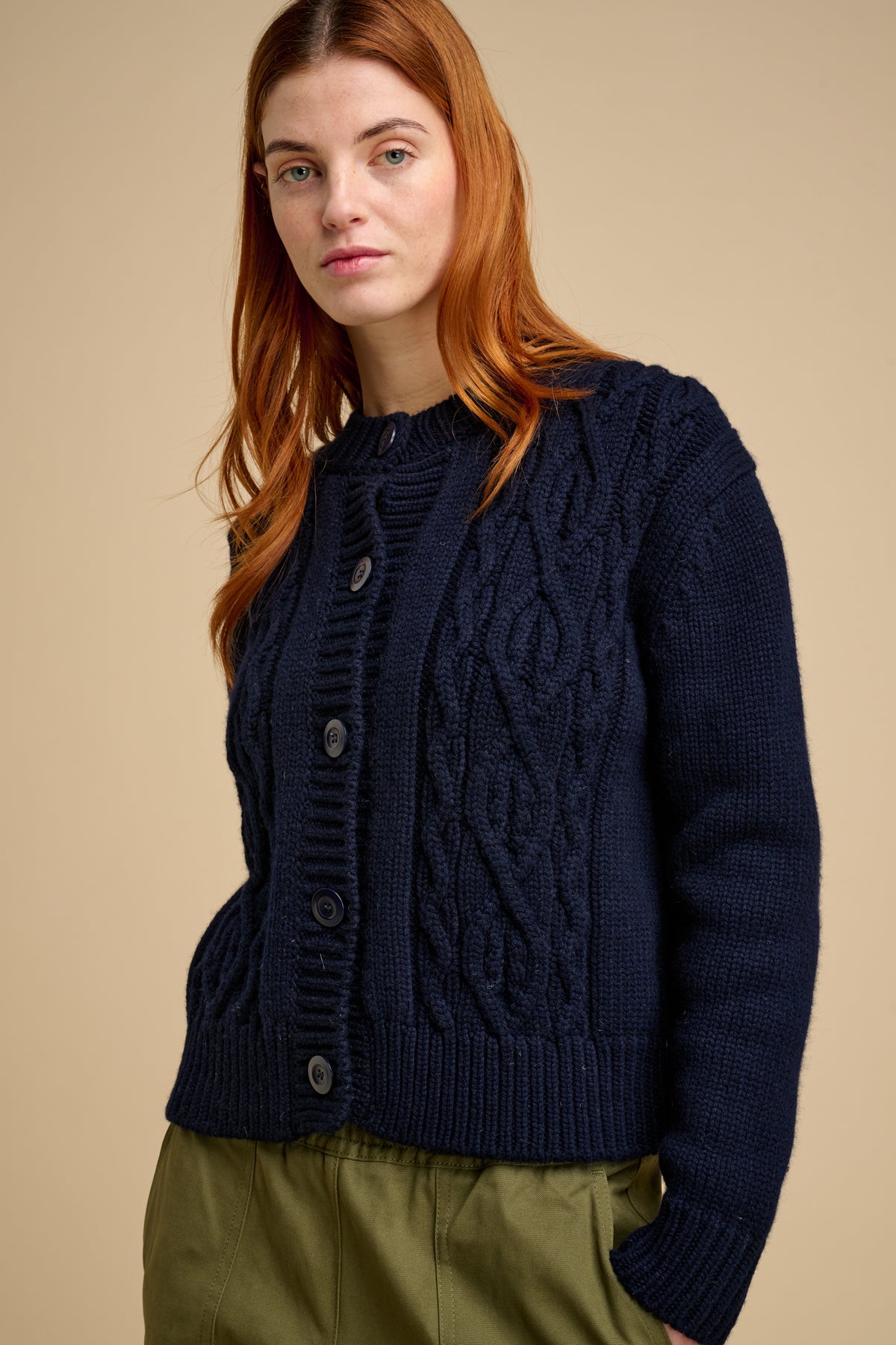 Woman wearing a navy blue cable knit cardigan against a beige background
