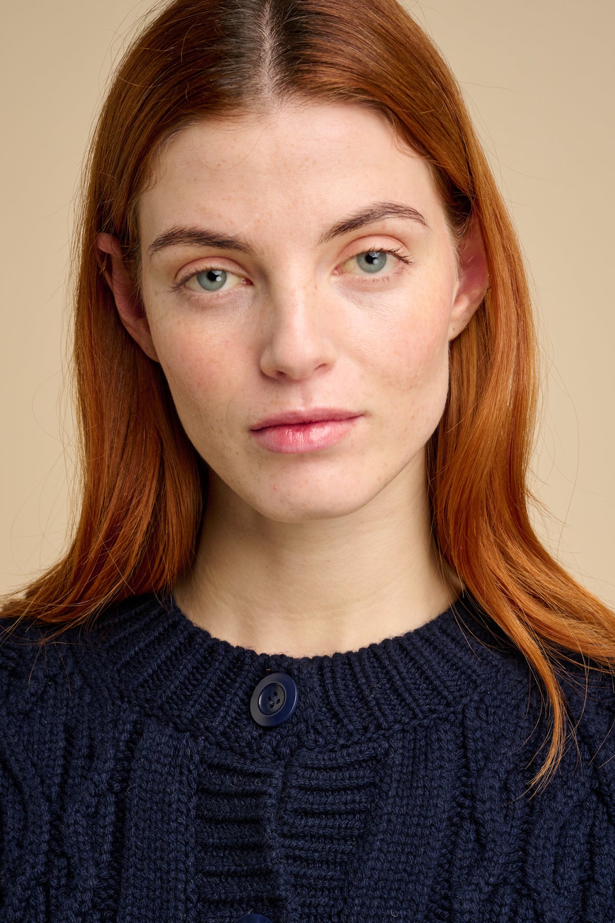 Woman wearing a navy blue cable knit cardigan against a beige background