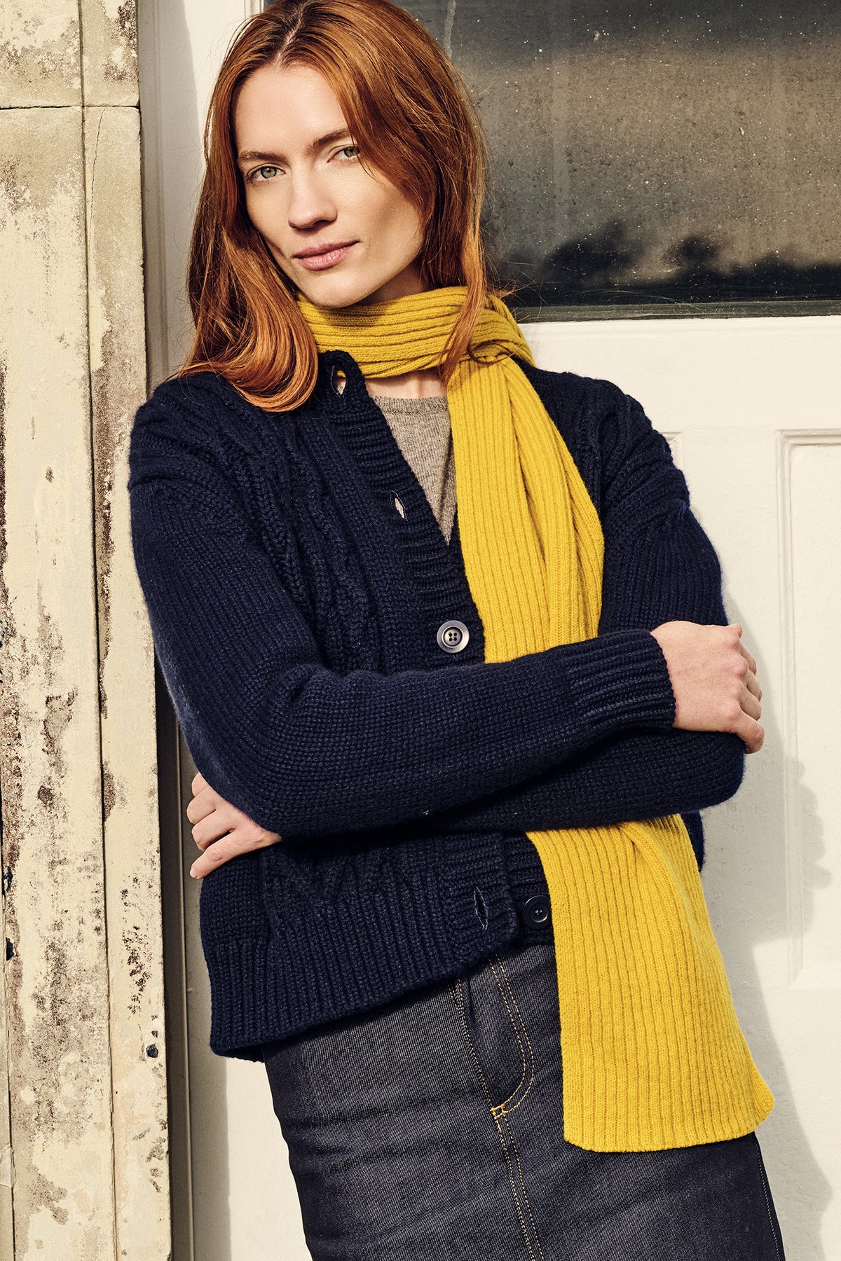 Woman wearing a navy cardigan and yellow scarf against a neutral background
