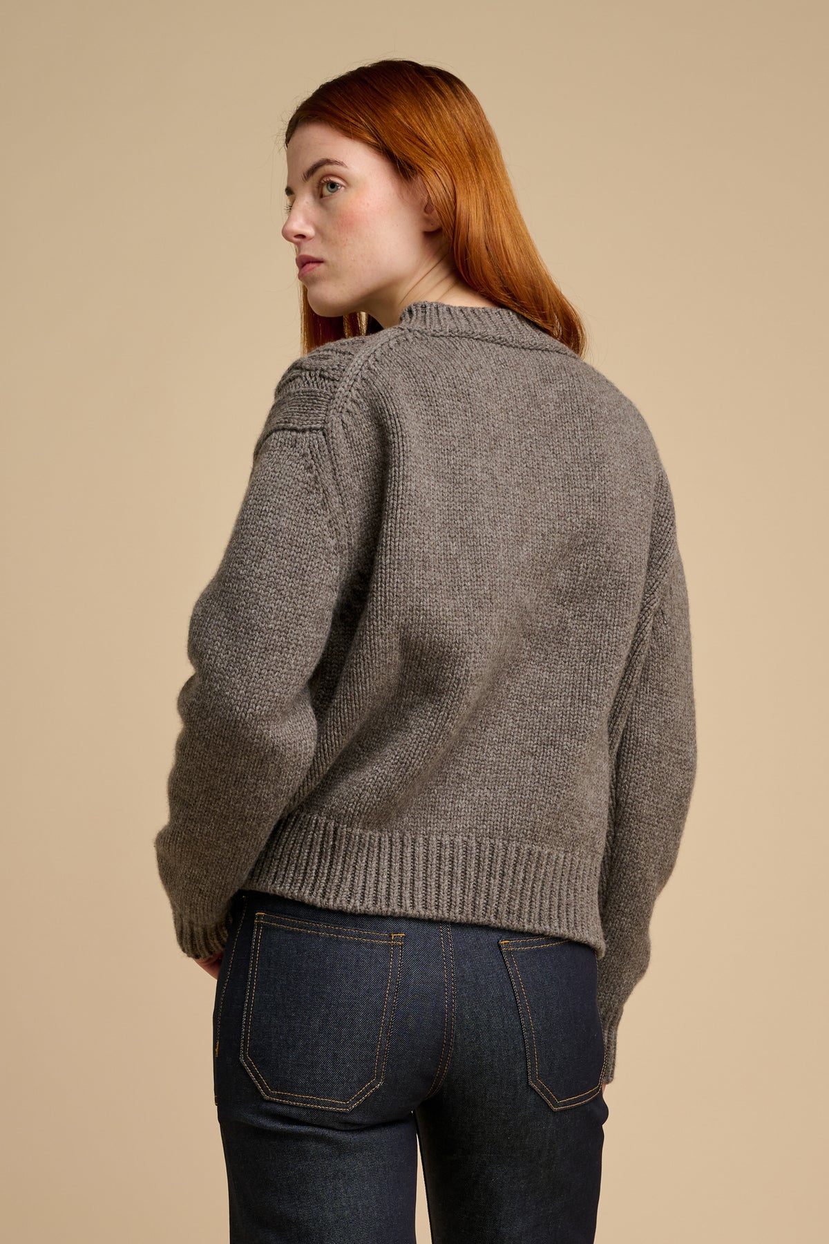 The back of woman wearing heavy cable knit cardigan in truffle.