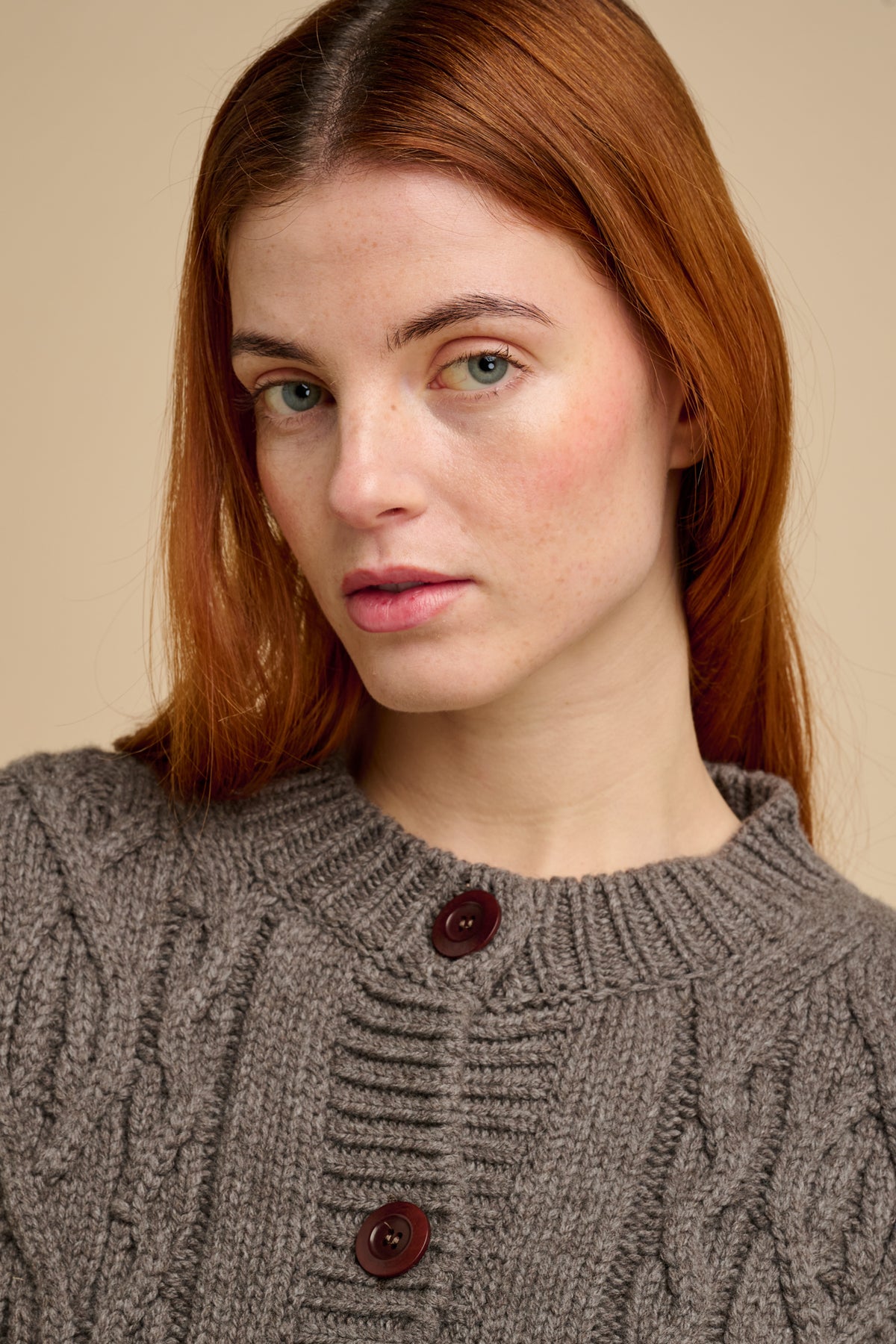 Woman wearing a truffle cable knit sweater with brown buttons against a beige background