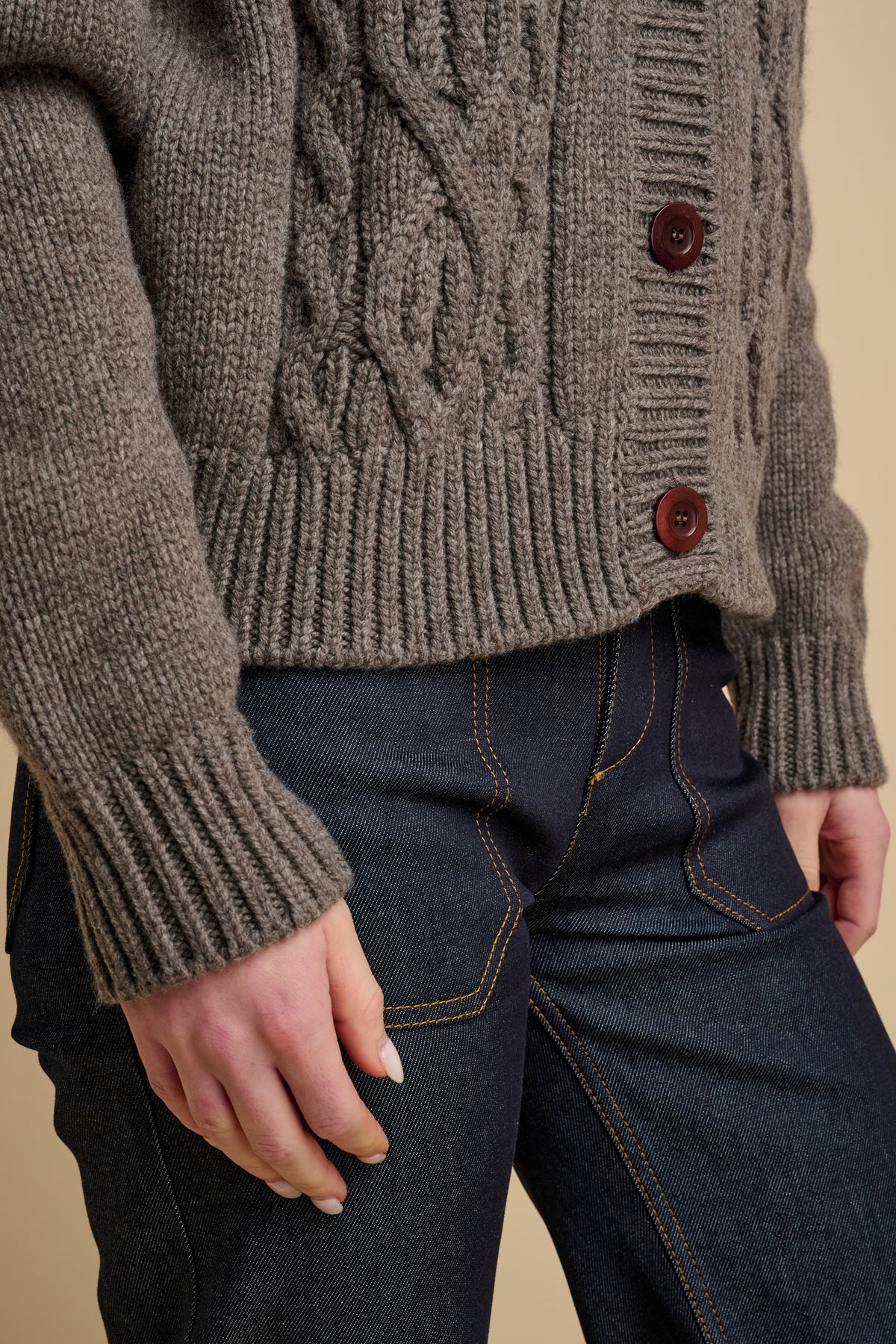 Woman wearing cable knit cardigan in truffle with indigo jeans.