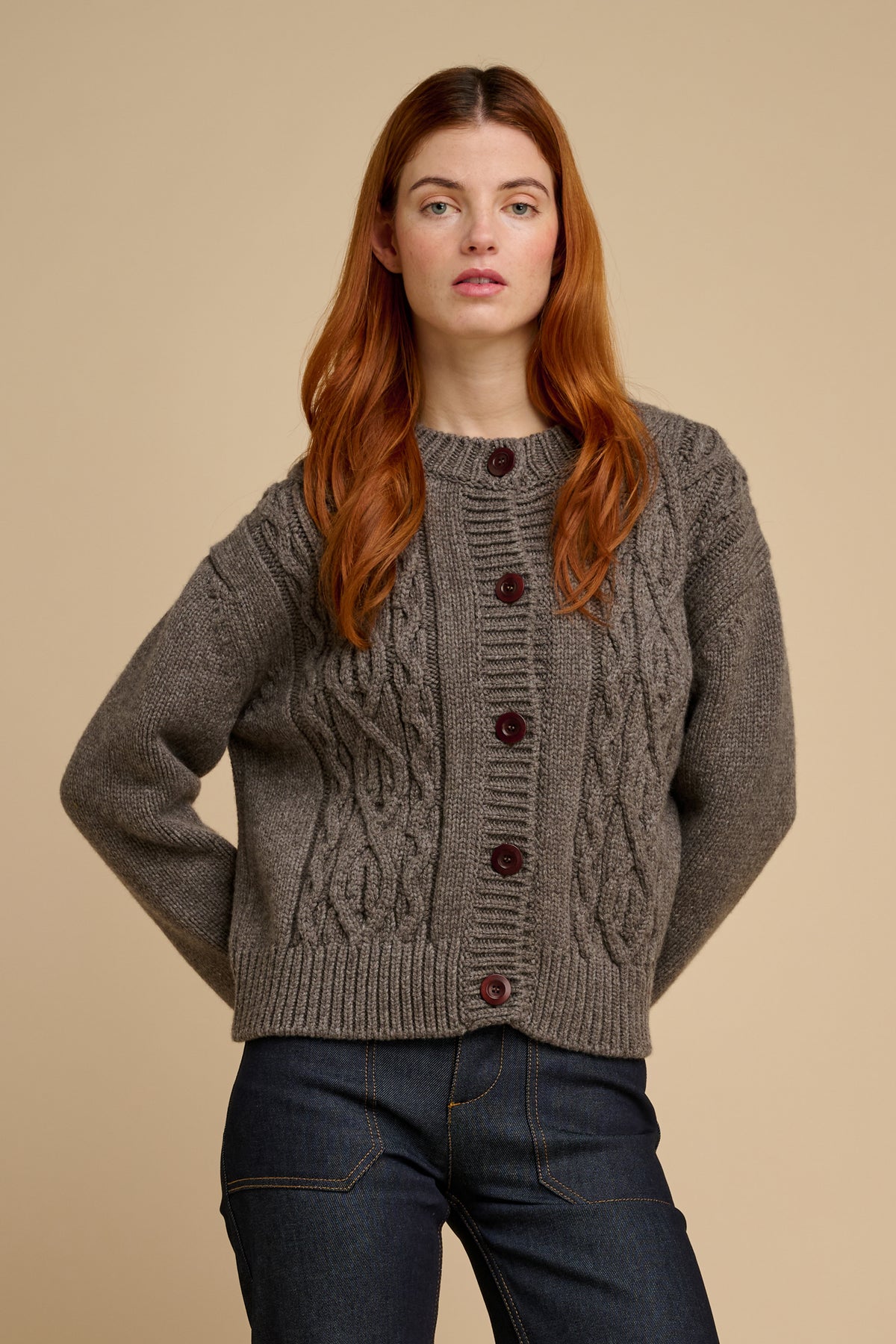 Woman wearing a truffle coloured cable knit cardigan with brown buttons on a beige background