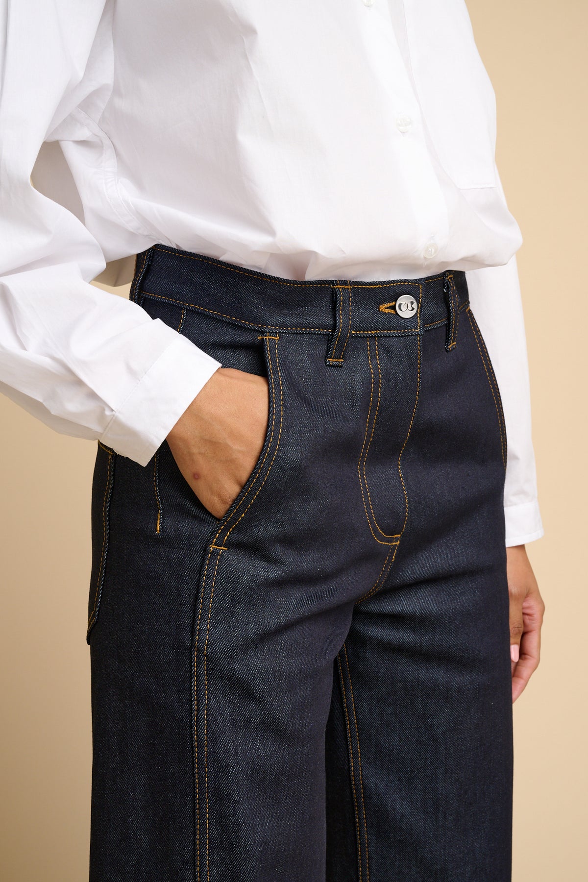 Female wearing indigo jeans and a white shirt against a beige background