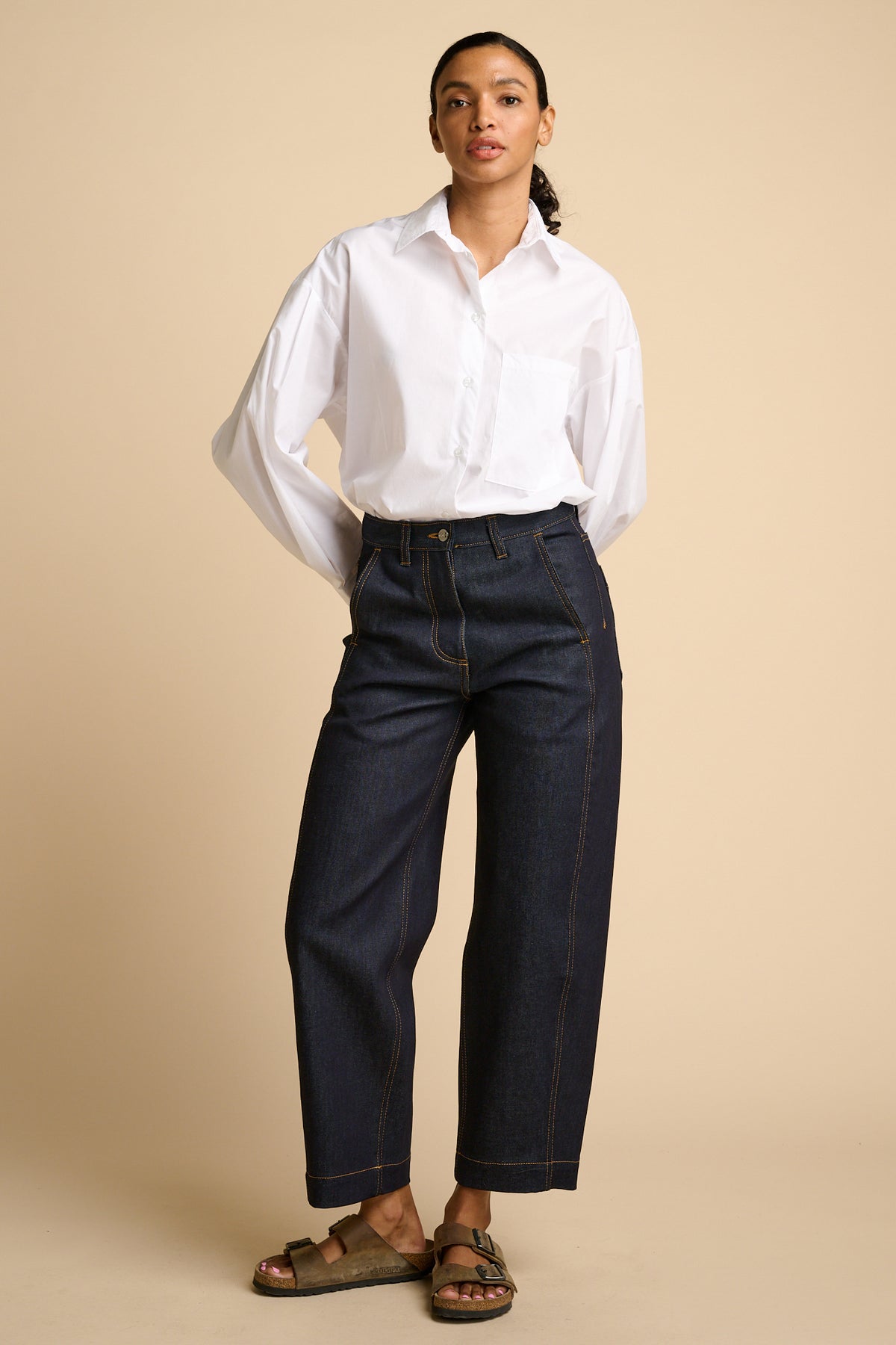 Woman wearing a white shirt and indigo jeans against a beige background