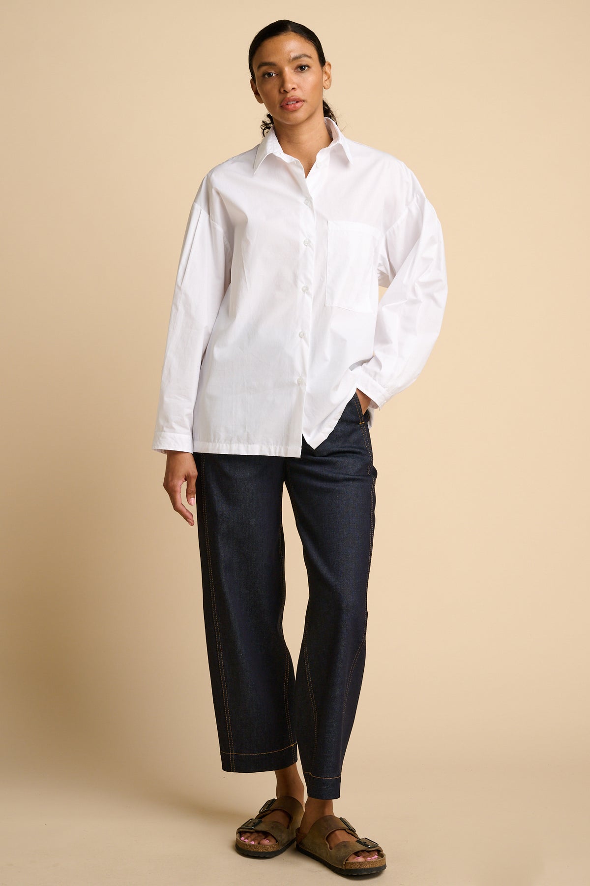 Woman wearing a white shirt and indigo jeans against a beige background