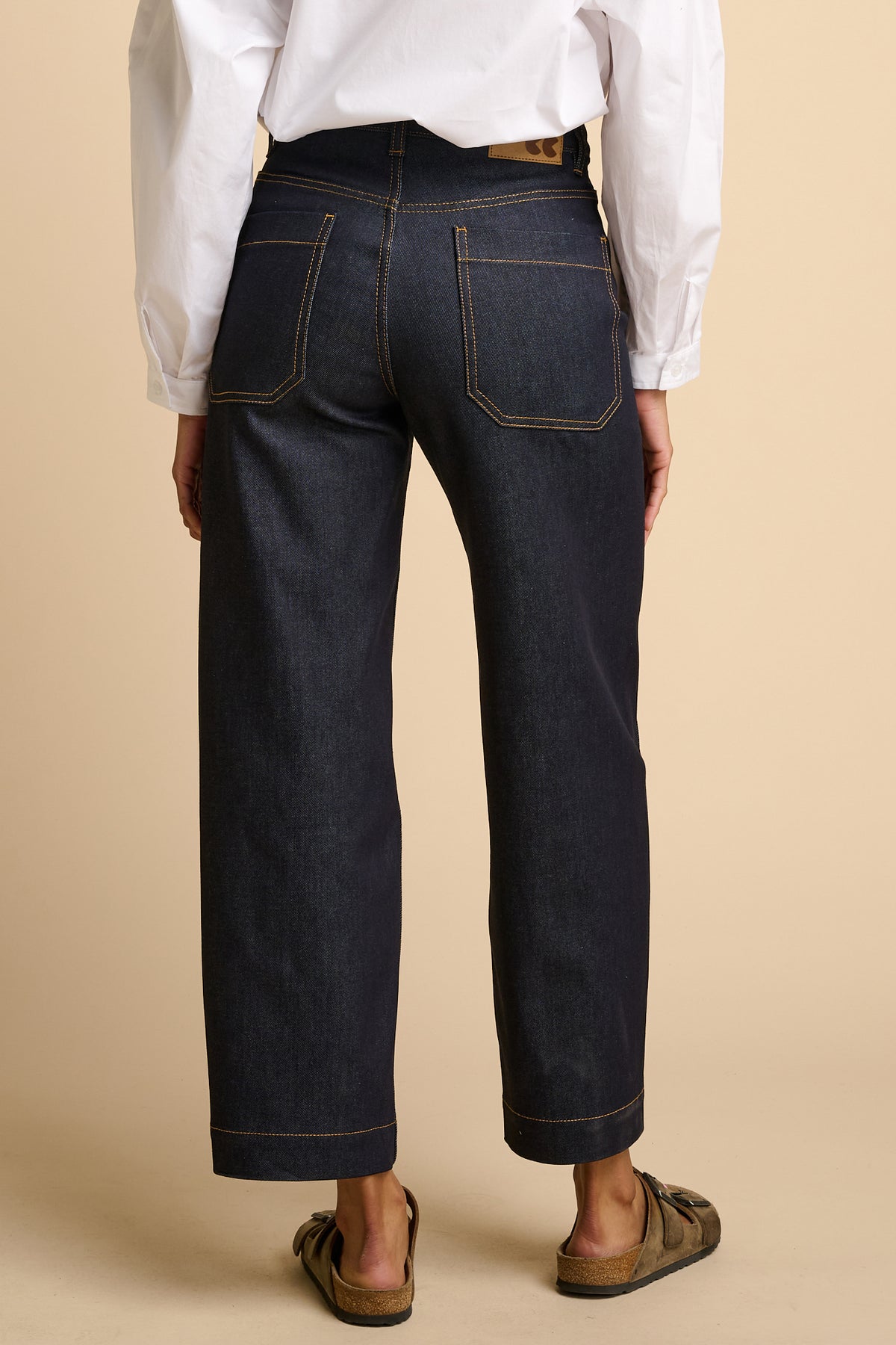 Female wearing indigo jeans and a white shirt on a beige background