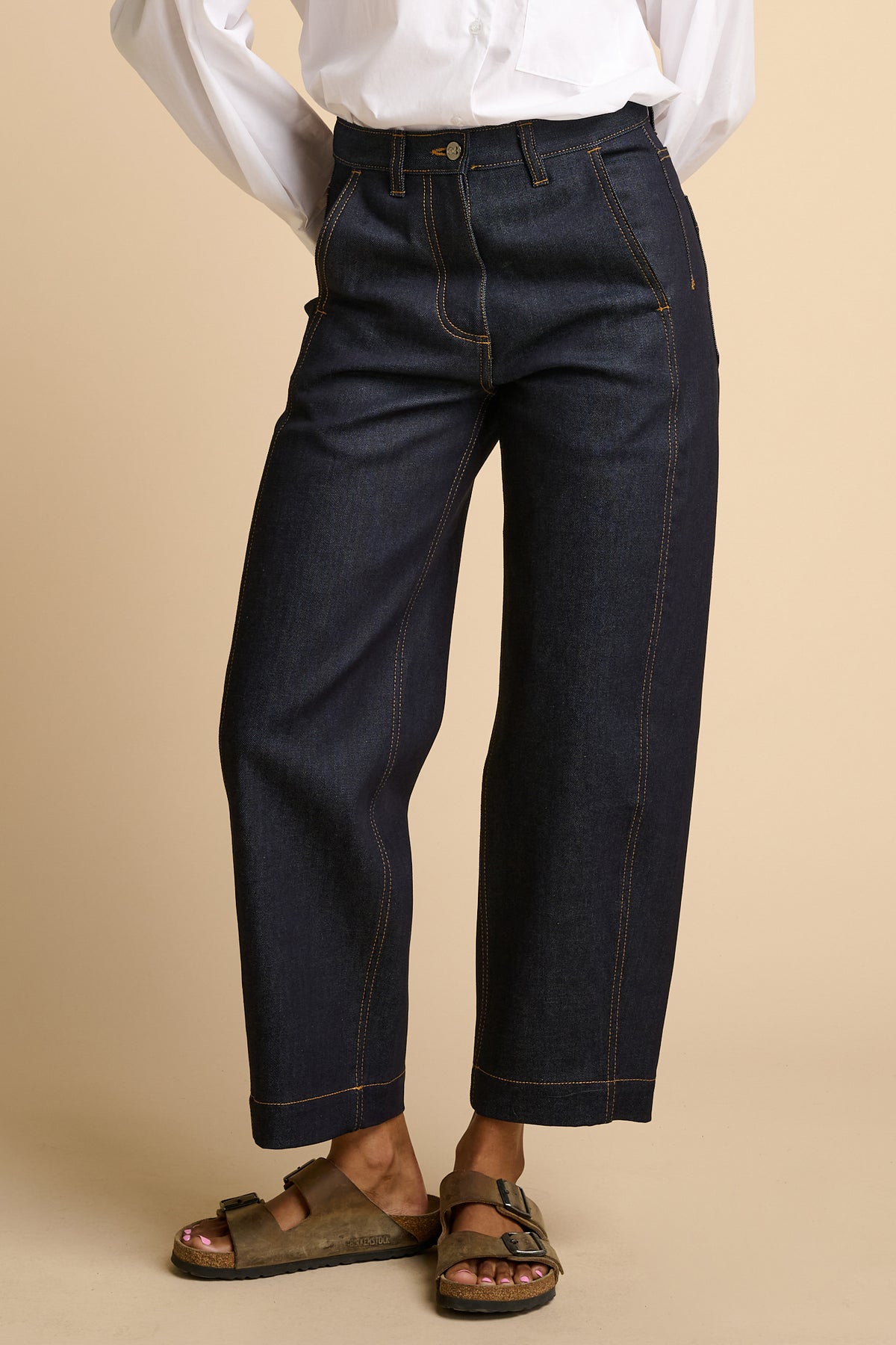 Female wearing indigo jeans and brown sandals on a beige background