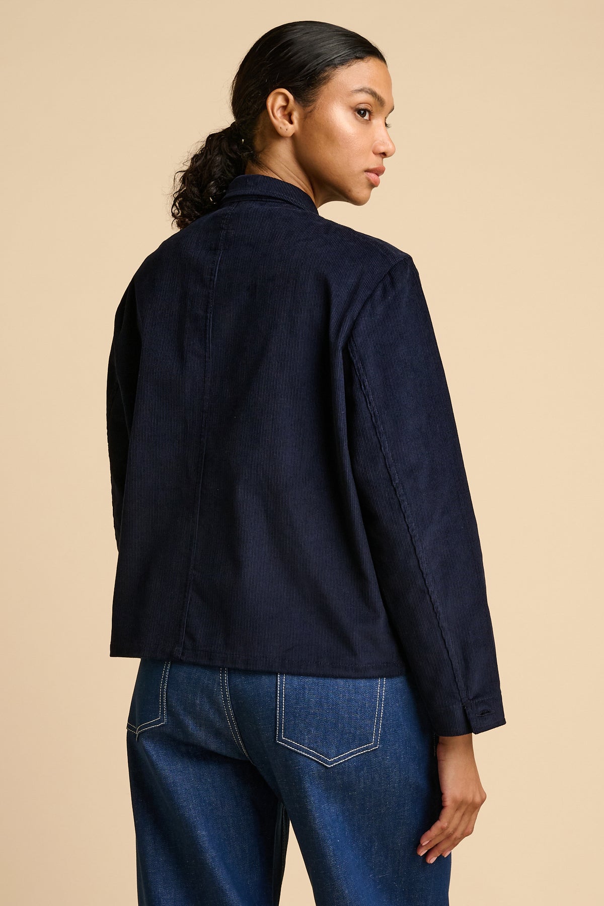 Woman wearing a navy overshirt and blue jeans on a beige background