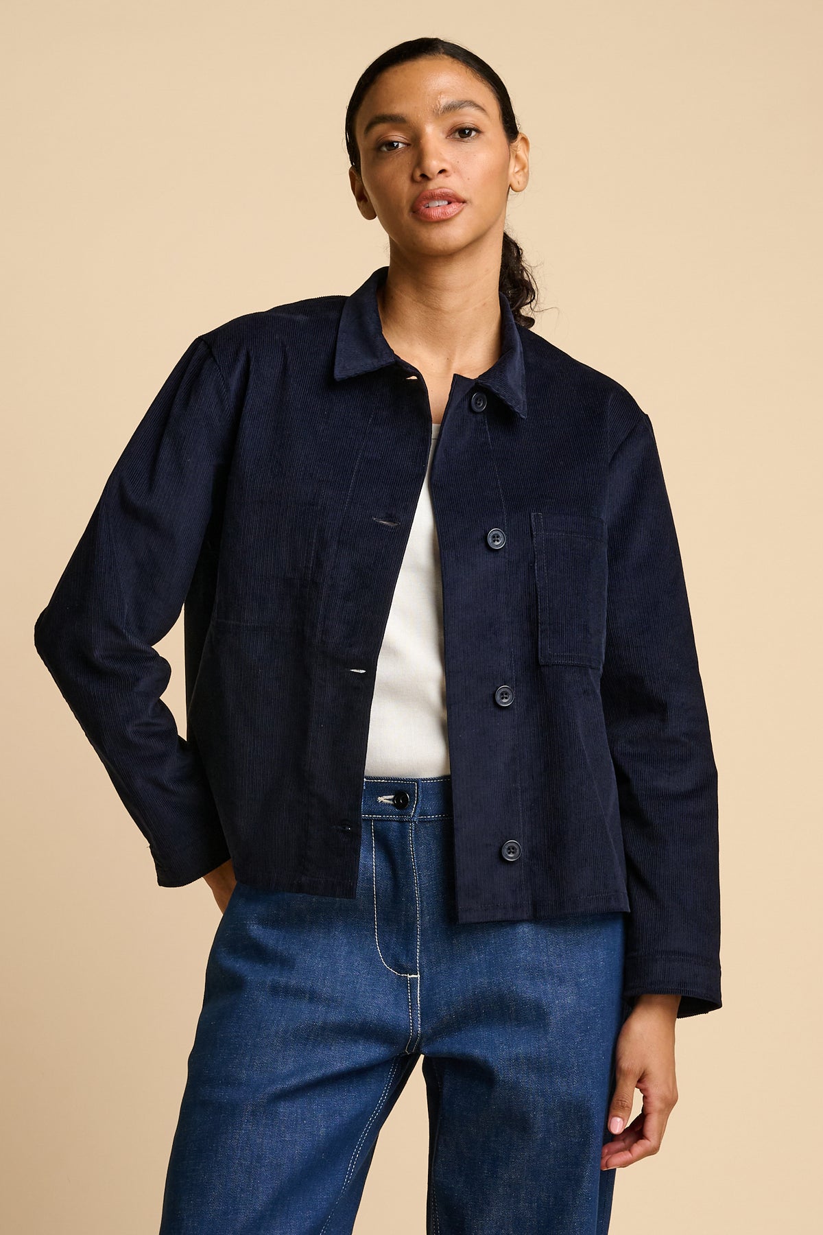 Woman wearing a navy overshirt and blue jeans on a beige background
