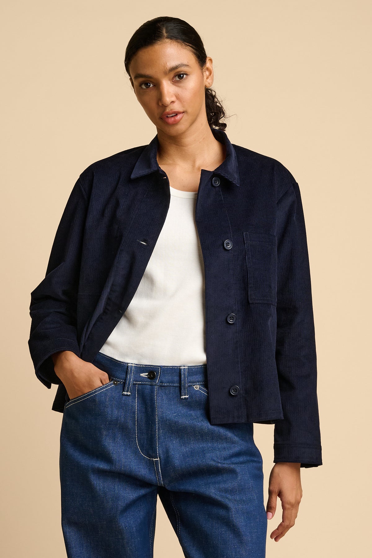 Woman wearing a navy overshirt and blue jeans on a beige background