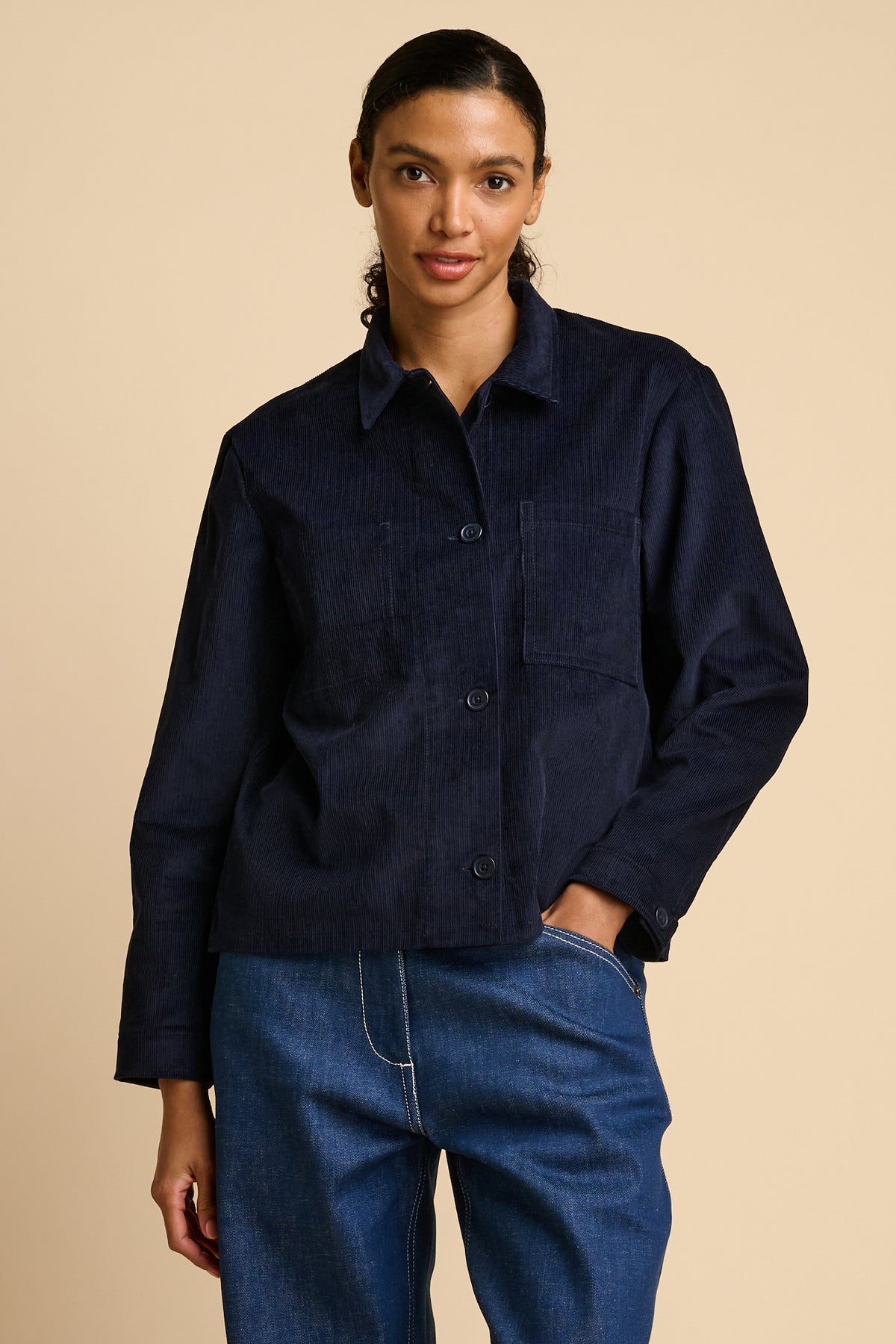 Woman wearing a navy overshirt and blue jeans on a beige background