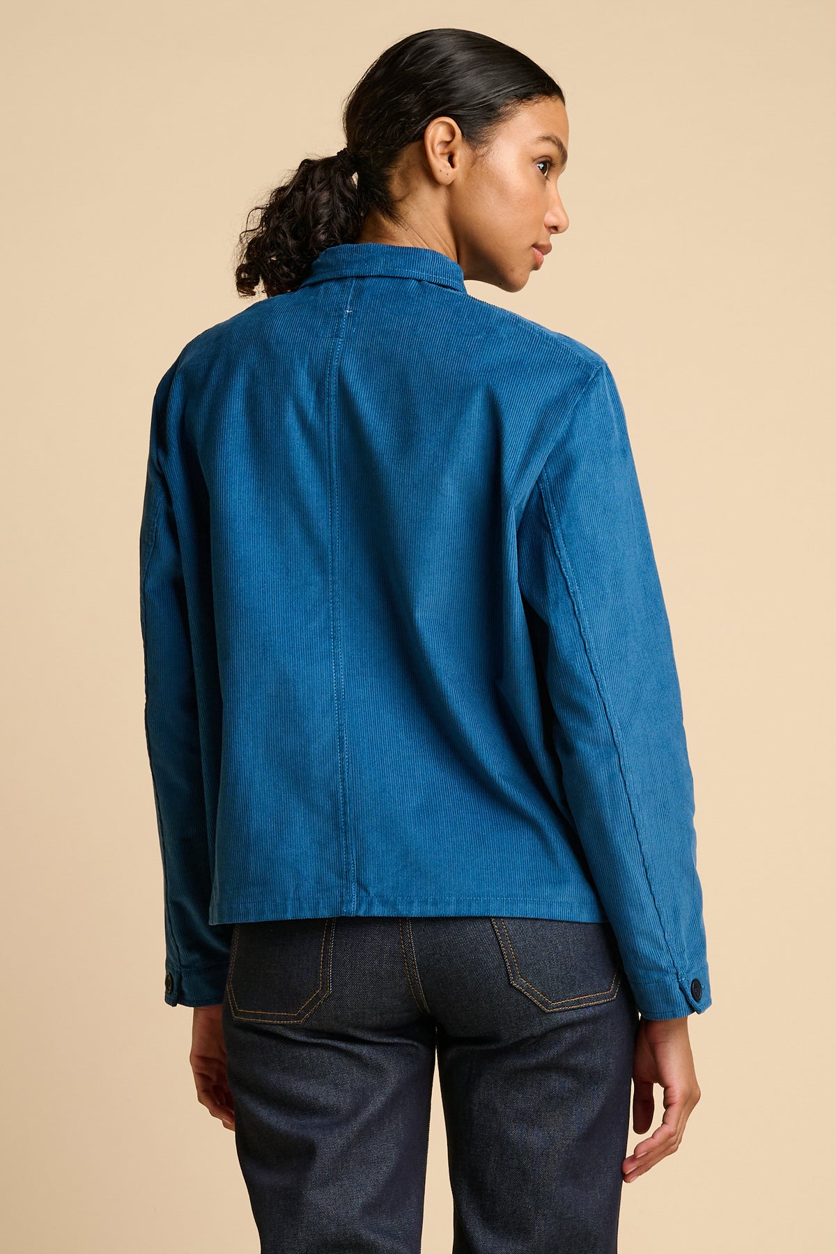 Woman wearing a blue jacket and indigo jeans on a beige background