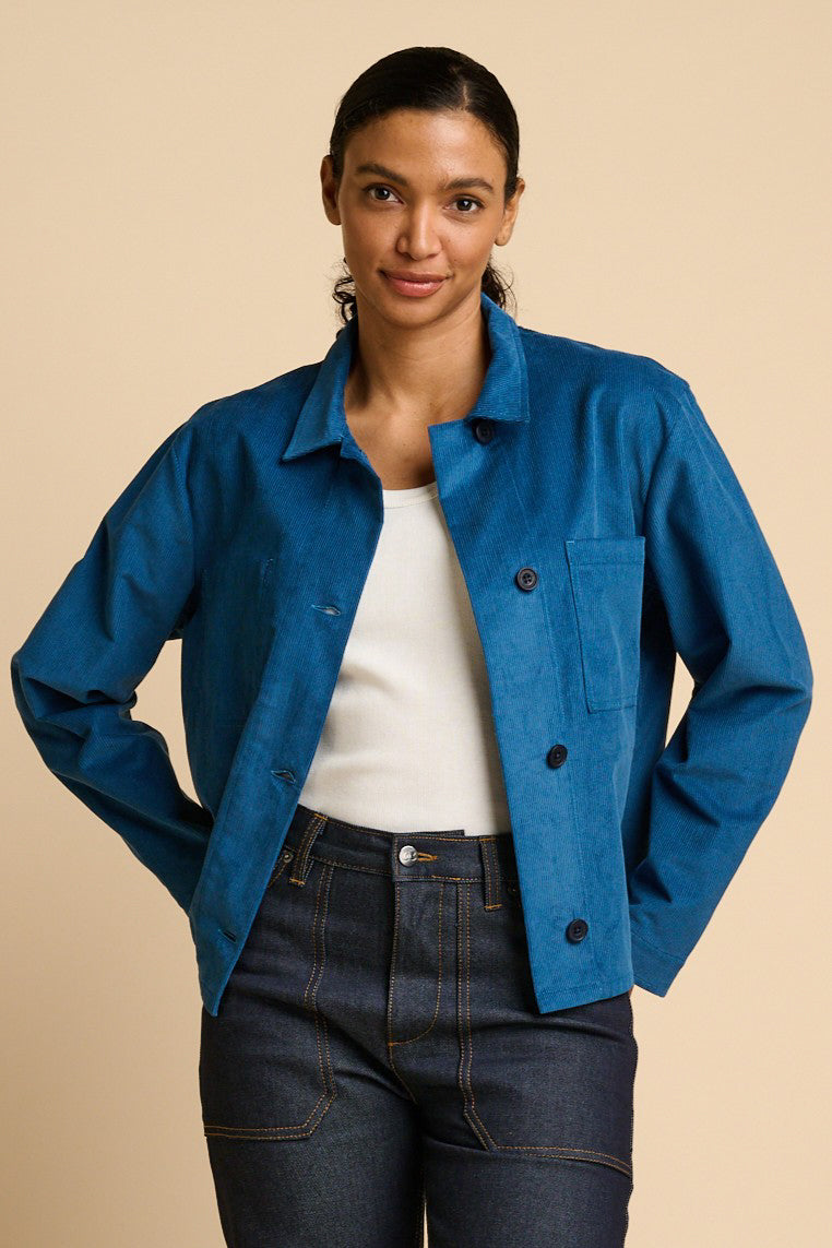 Woman wearing a blue jacket over a white top and indigo jeans on a beige background