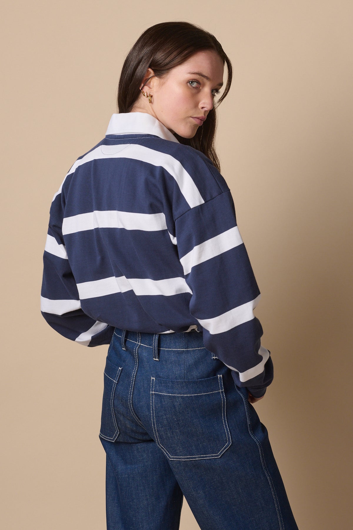 Female wearing fine stripe rugby shirt in navy white turned away, looking  back to camera