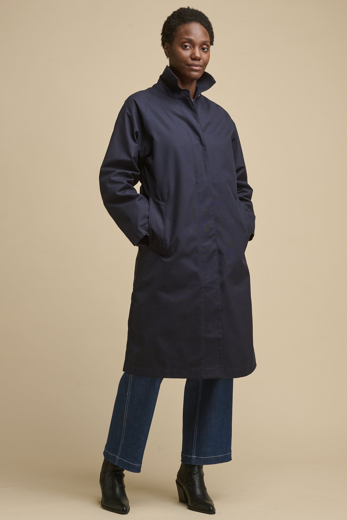 Full body image of female wearing women's Frances Raglan Belted Raincoat in navy with hands in two front pockets