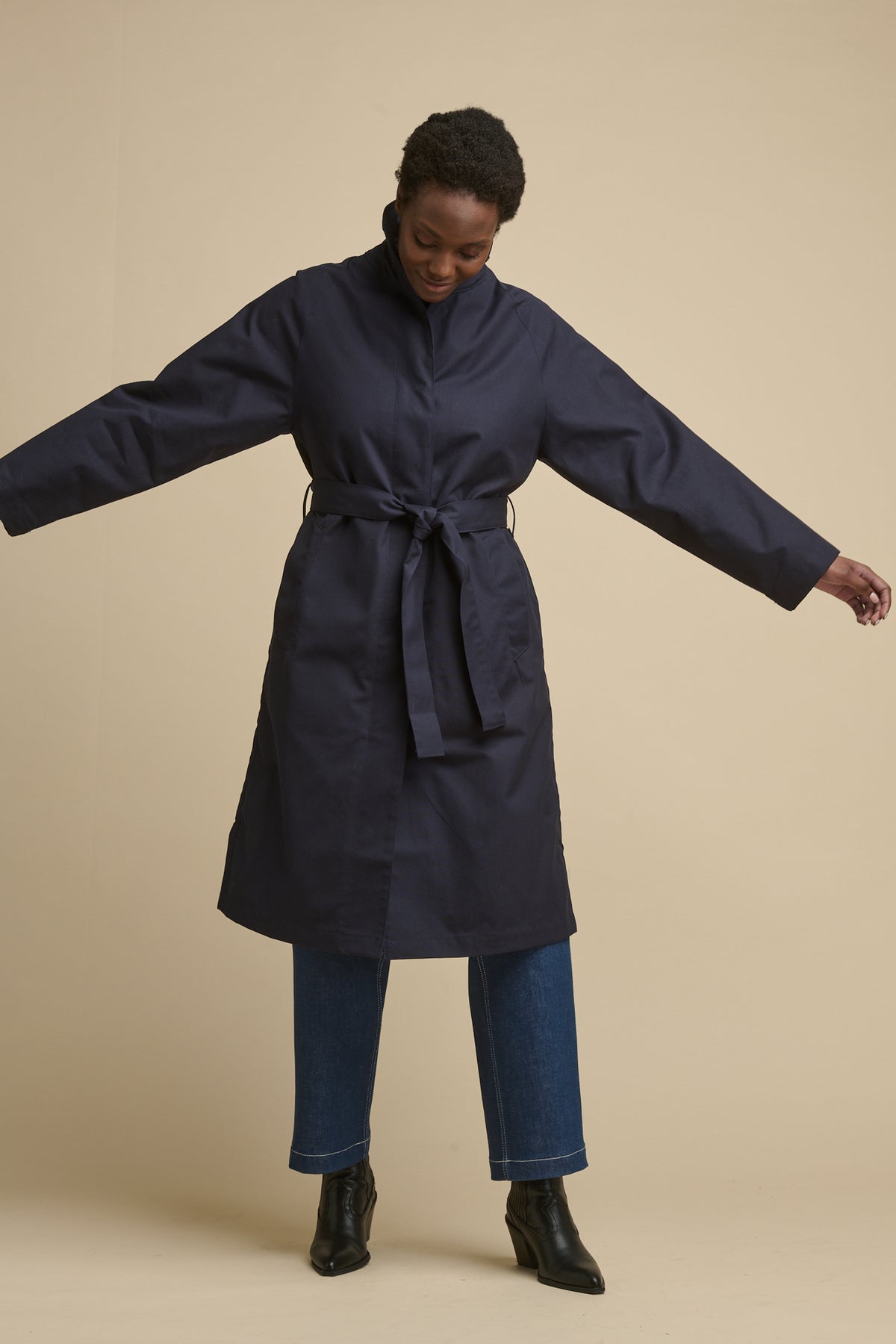 Full body image of female wearing women's Frances Raglan Belted Raincoat in navy with belt tie fastened around the waist 